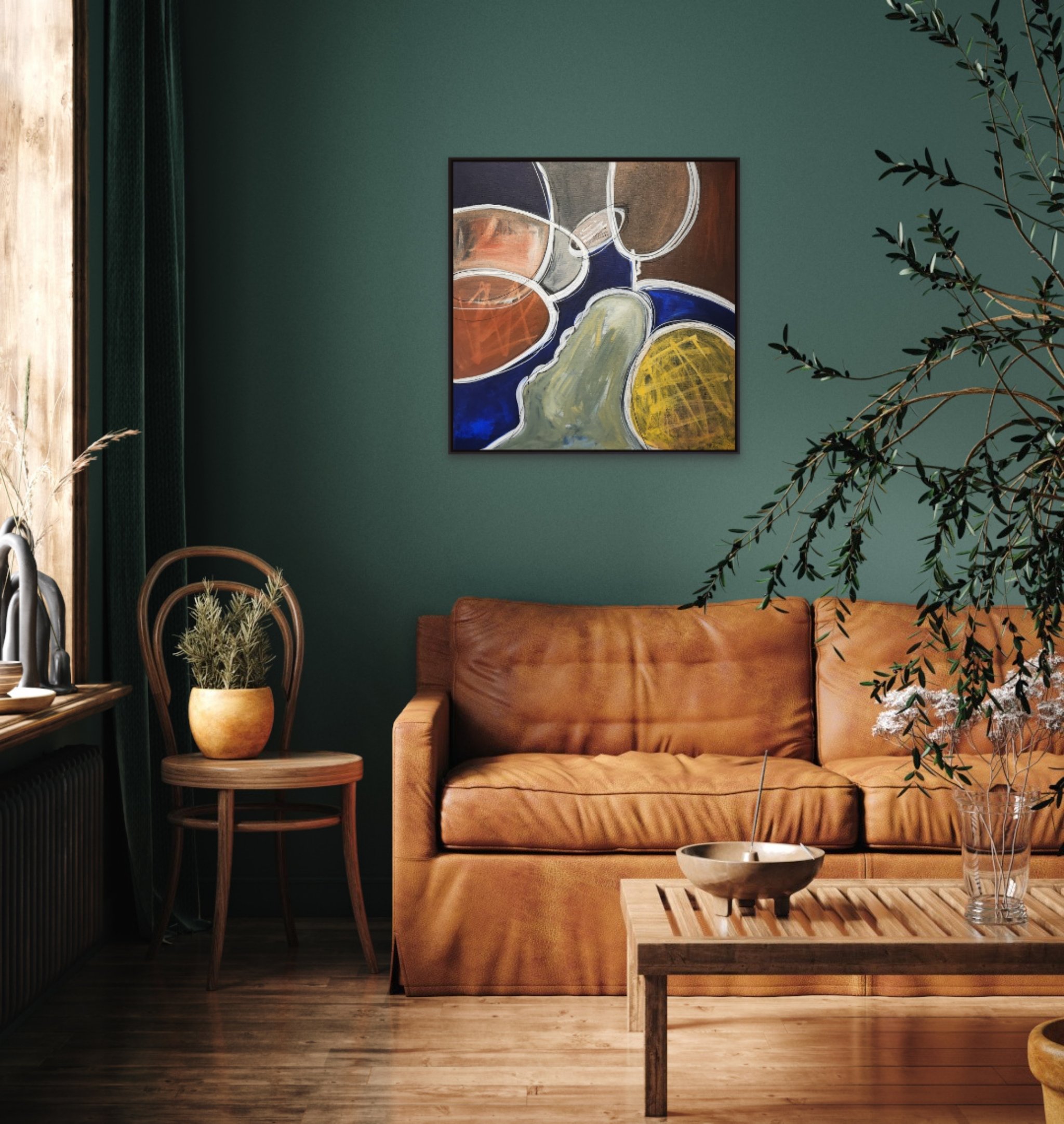A cozy living room corner with a brown leather sofa, a small wooden side table holding a potted plant, and a wooden coffee table with a bowl and glass of water. A large abstract painting with circular patterns is on a dark green wall, and part of a plant is visible in the foreground on the right.