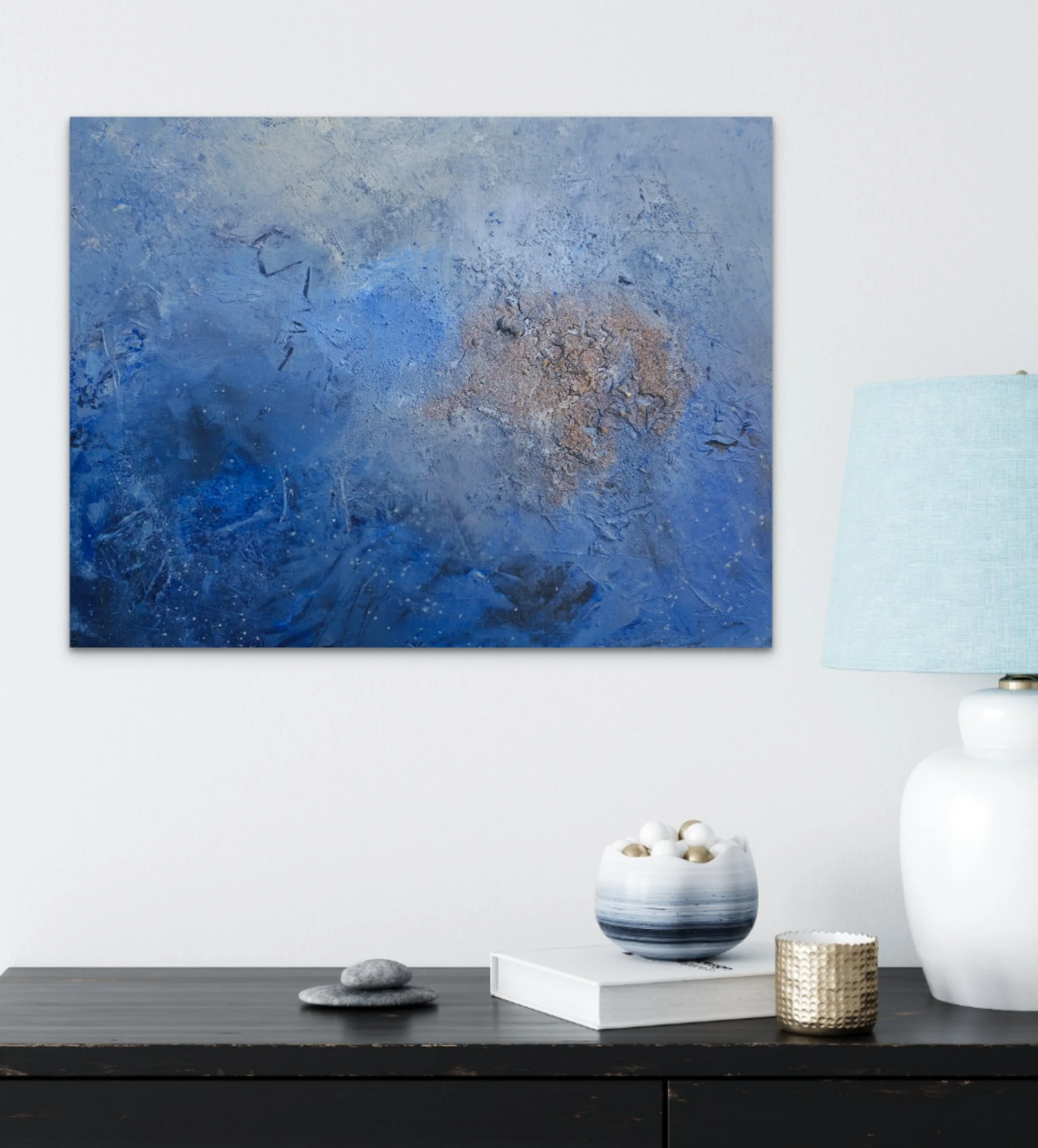 Minimalist home decor with abstract blue and beige painting on white wall above black wooden sideboard. On the sideboard are a white and navy striped vase with neutral-colored balls, a textured beige jar, and three gray stones. There is a white tray underneath the vase.