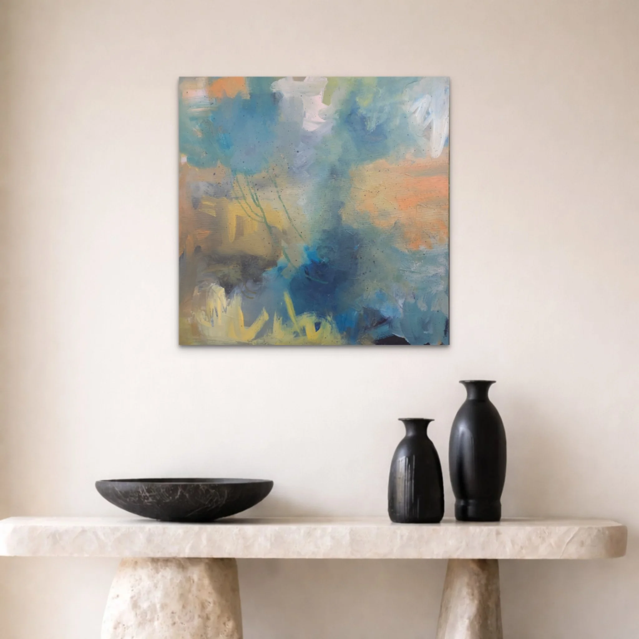 A symmetrical display of decorative objects on a shelf, including vases in shades of black, brown, and cream, with a black bowl, and a framed abstract painting with blue, green, and pastel colors against a beige wall.