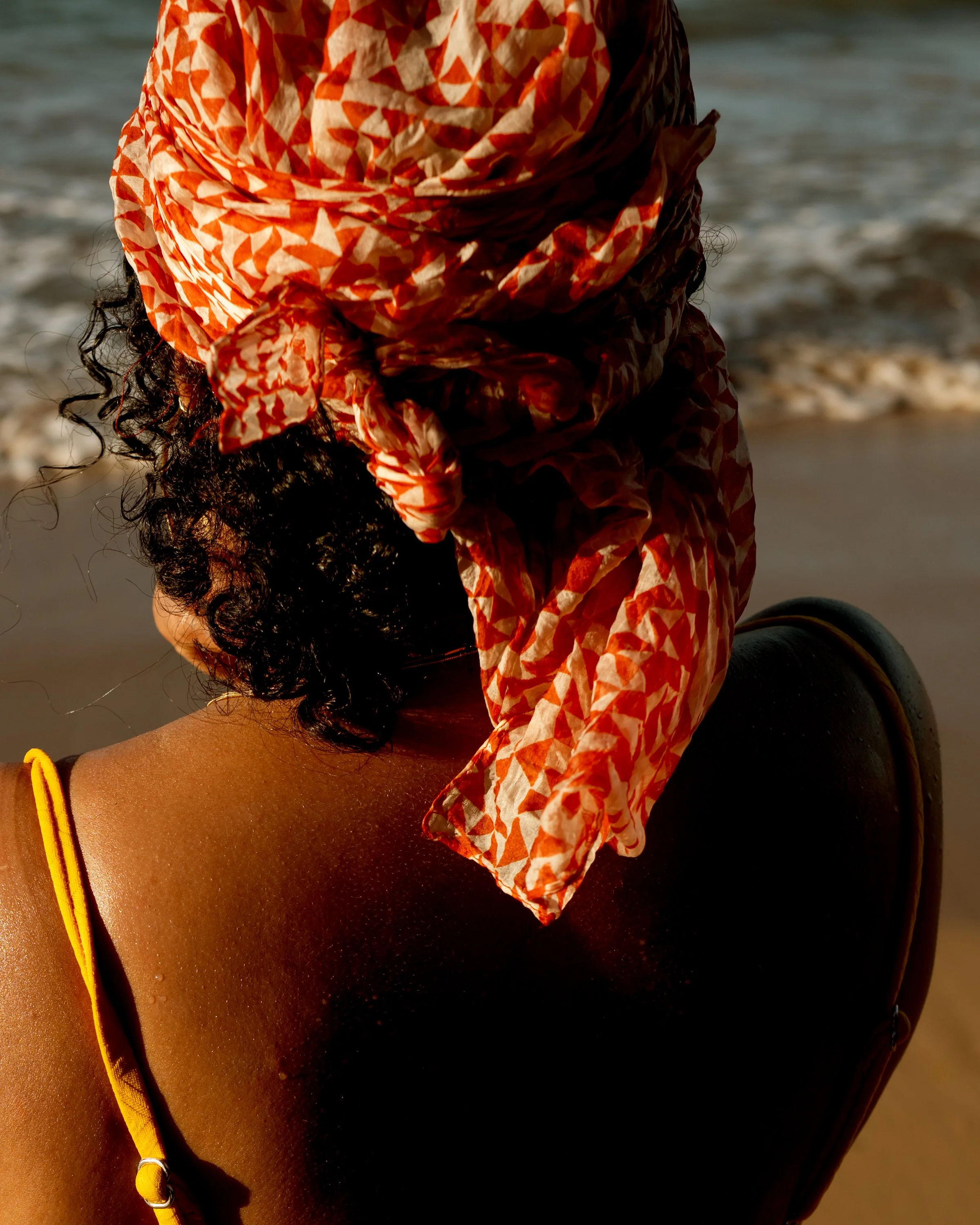 A person wearing a colorful headscarf standing by the water at the beach.