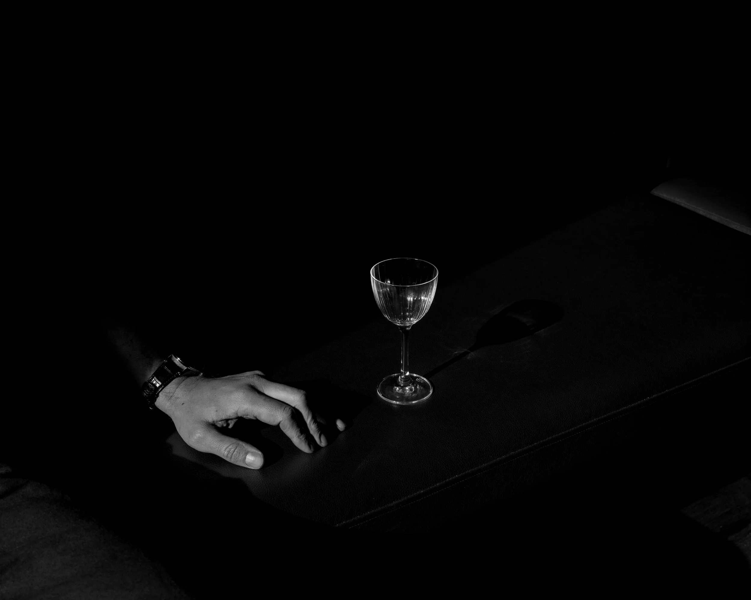 Black and white photo of a hand resting on a dark surface near an empty wine glass with a long stem.