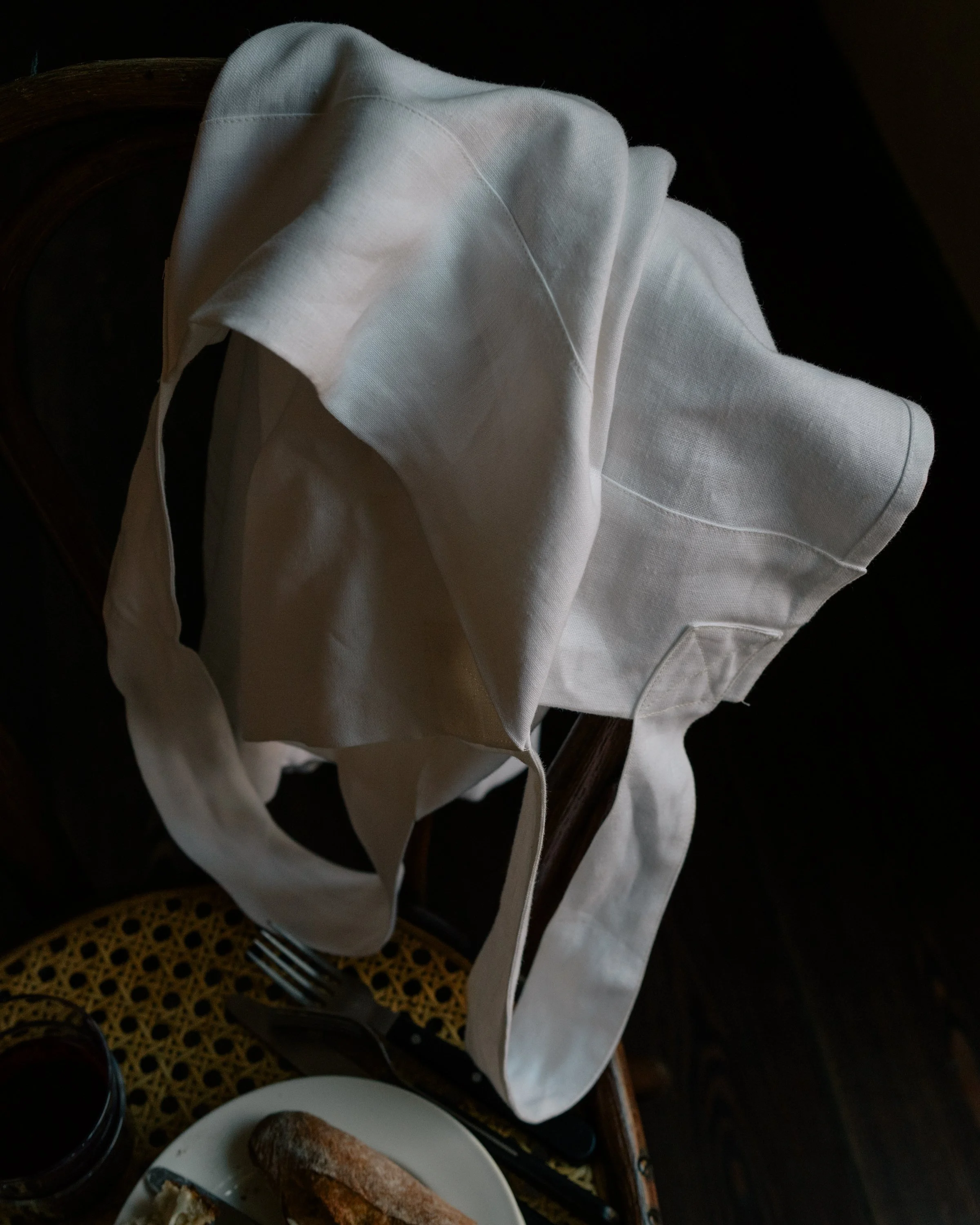 A white cloth napkin on a wooden table with a plate of bread, a glass of red wine, and a small dish of butter.