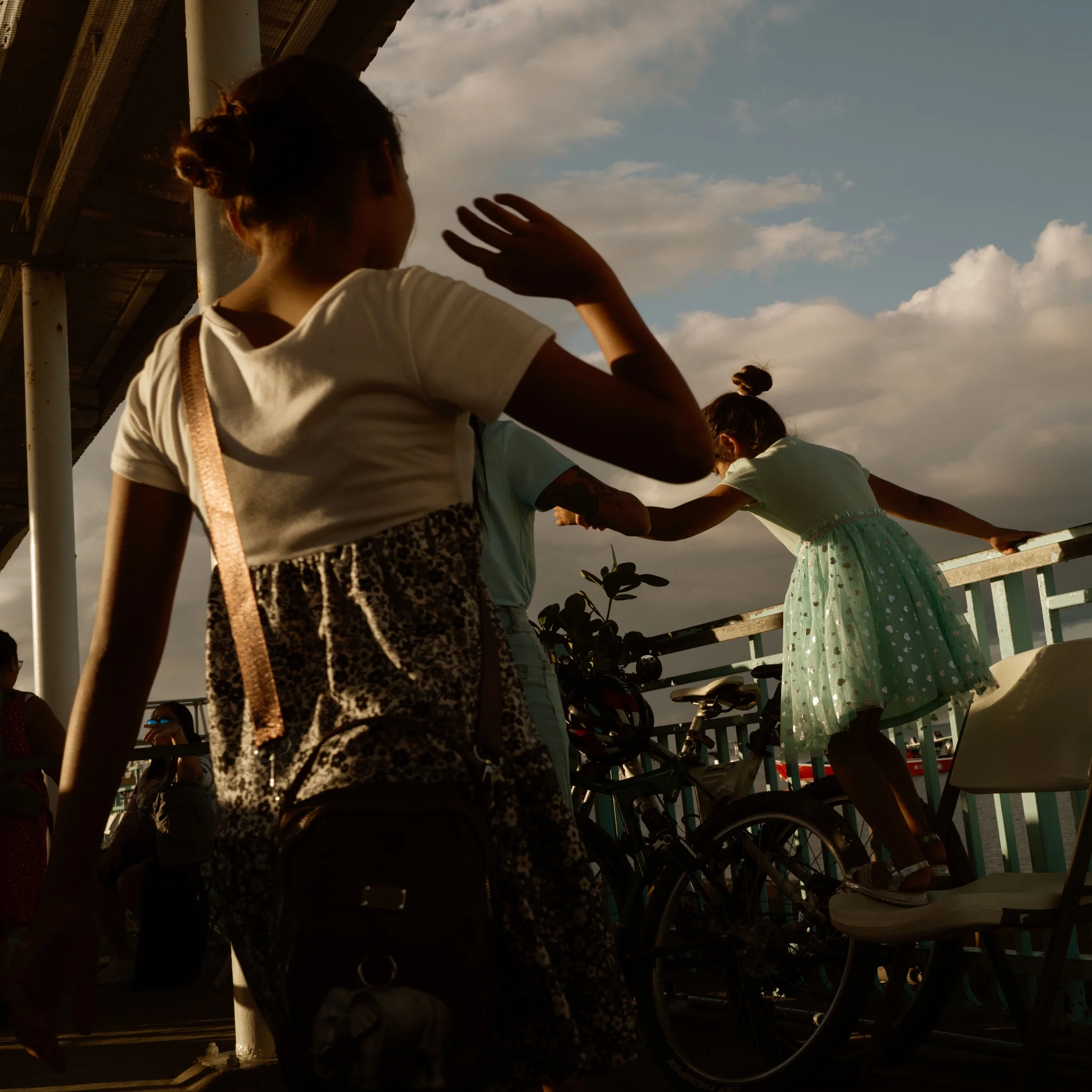 Silhouette children playing near bicycles under a bridge with a cloudy sky background.
