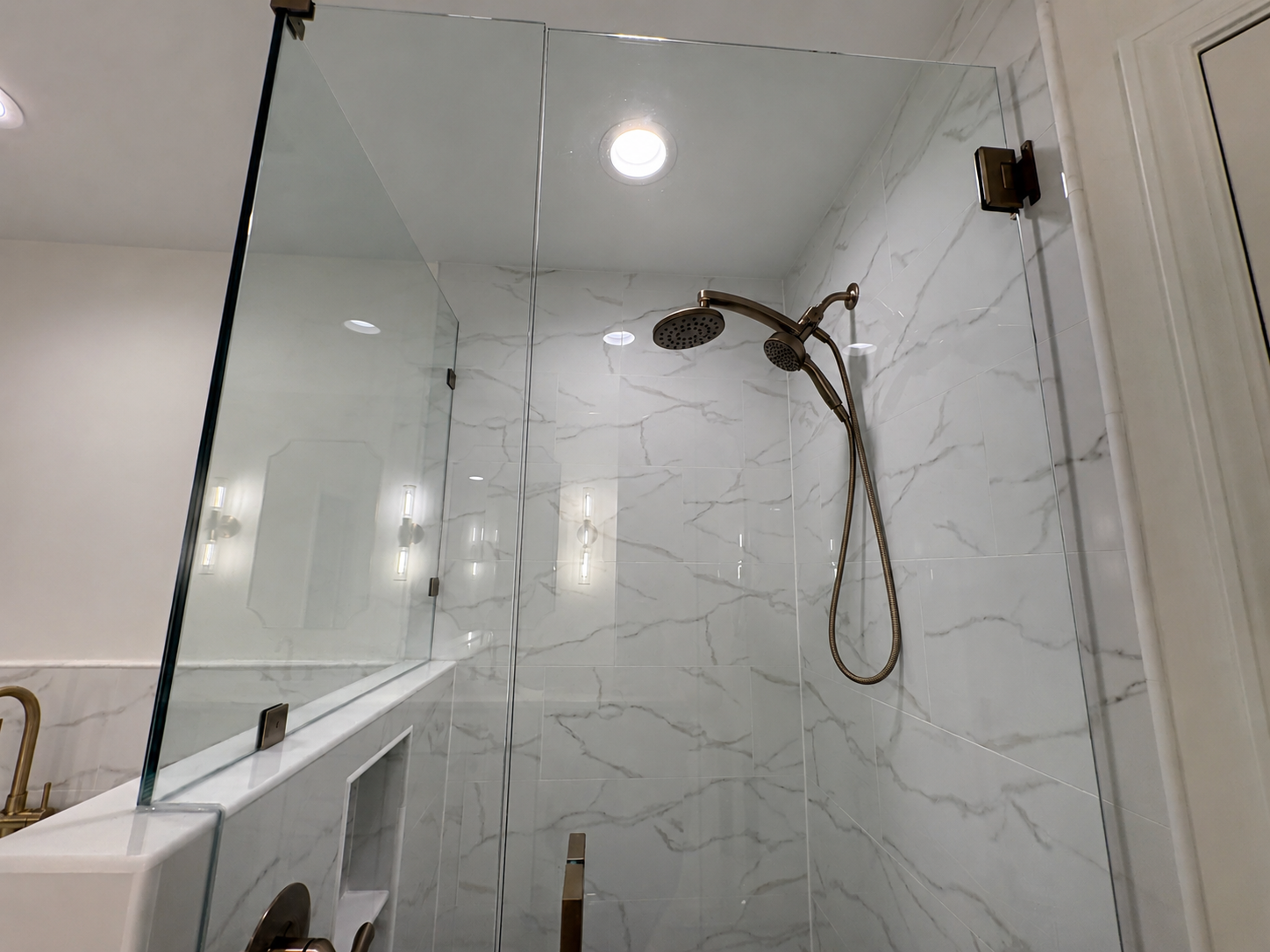 A frameless glass shower with floor-to-ceiling marble-look tile and brushed gold fixtures creates an elegant focal point in this luxury Jacksonville condo bathroom remodel by Elite Construction of JAX.