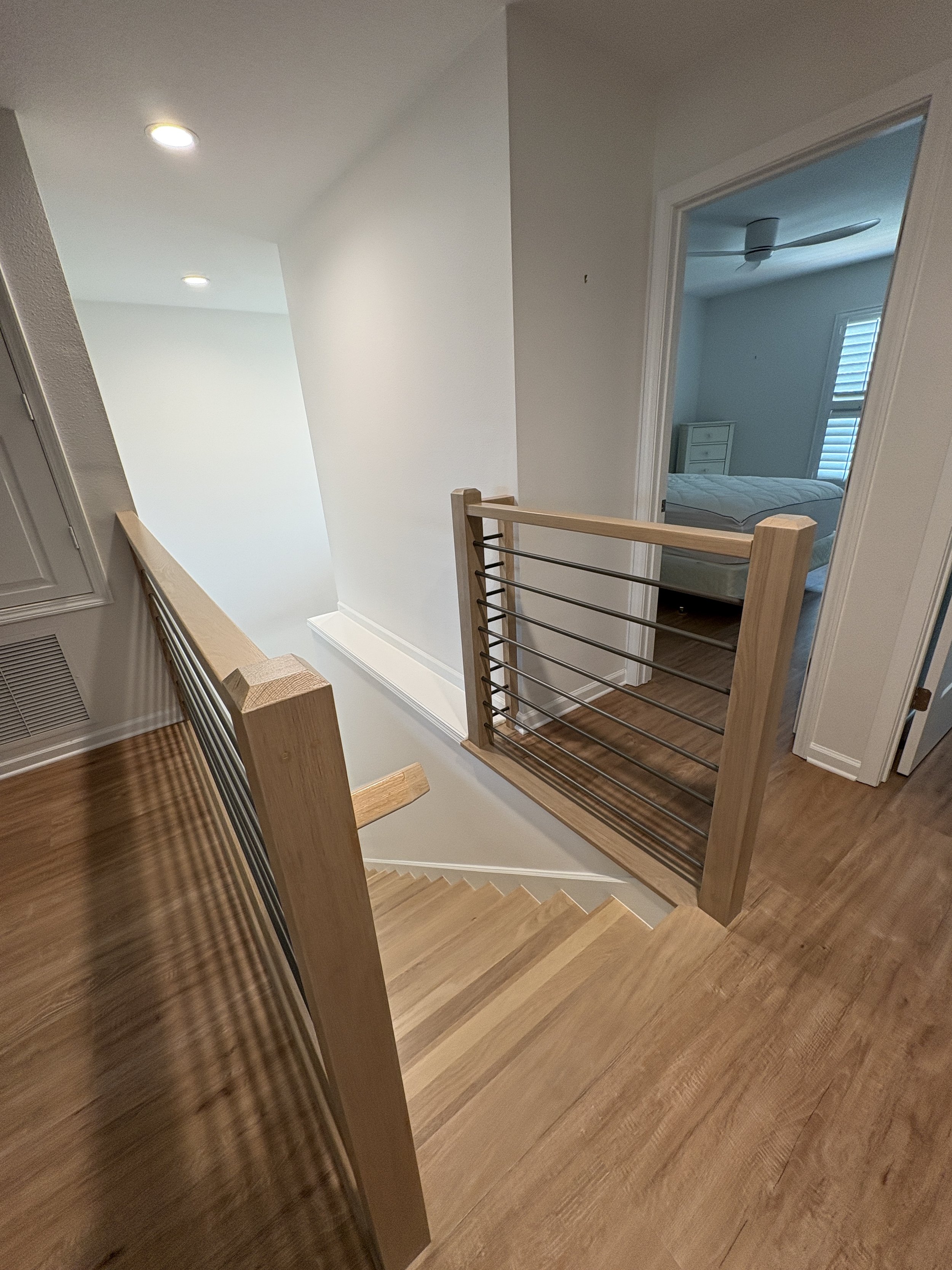 A modern horizontal metal balusters paired with natural wood handrails and stair treads gives this high-end Jacksonville condo remodel a clean, contemporary look. This custom staircase renovation was completed by Elite Construction of JAX.