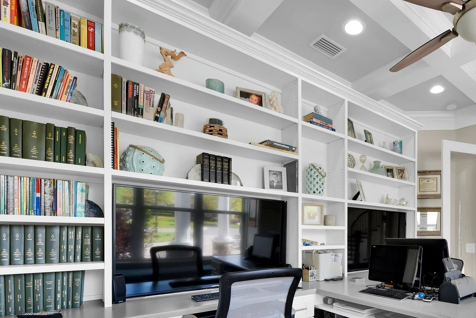 A large white bookcase filled with books, decorative items, and framed photos, with a large television and computer setup in front.