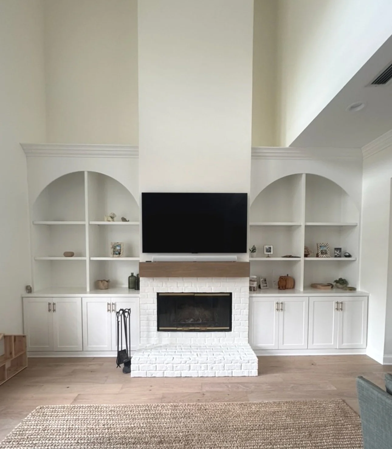 Living room with built-in white shelves surrounding a white brick fireplace and a mounted black flat-screen TV above it.