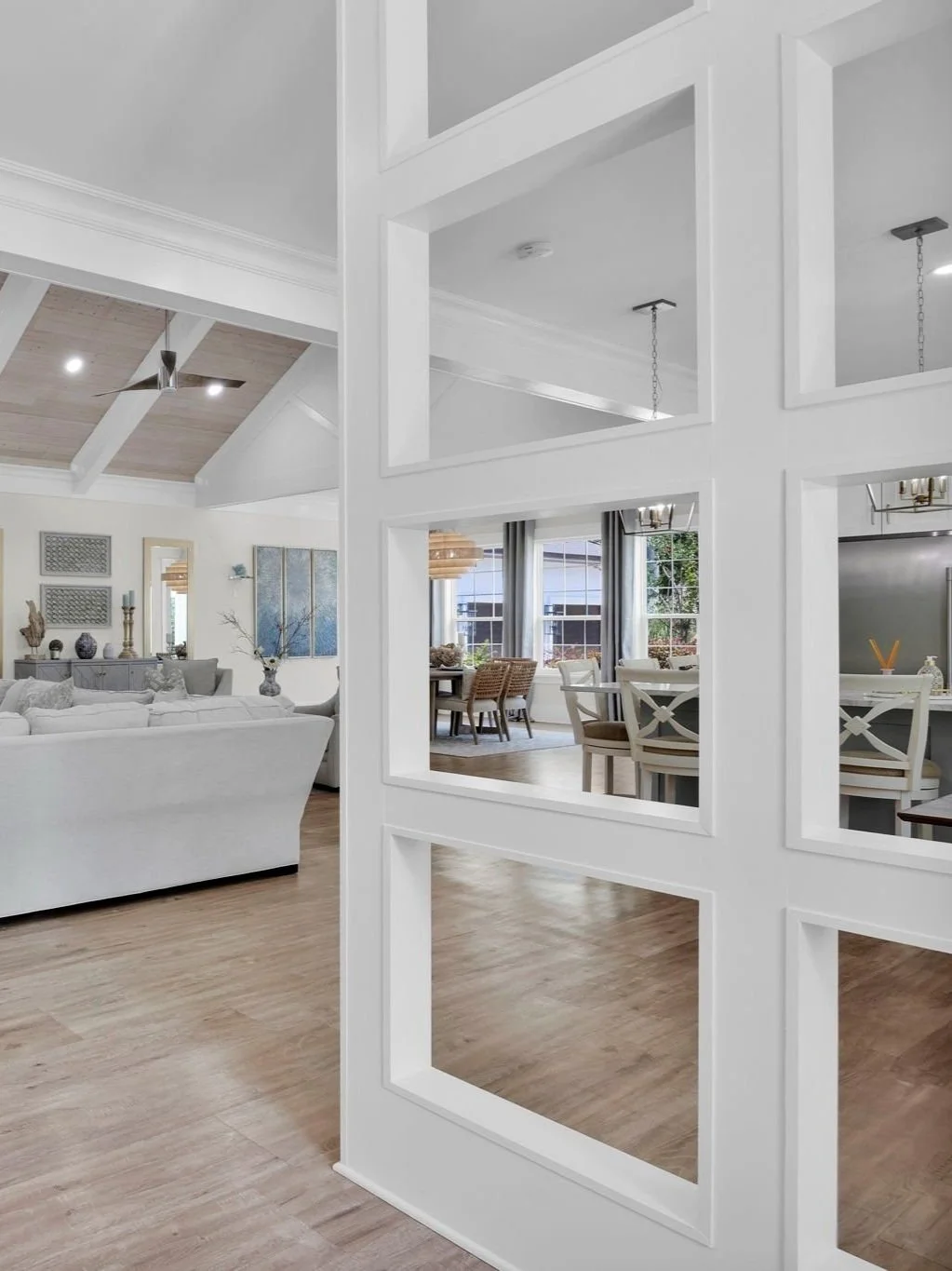 Open-concept living and dining area with white walls, wood flooring, and large windows, separated by a decorative white partition with square openings.