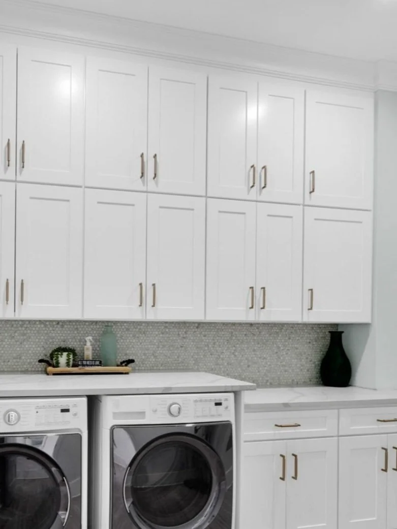 Laundry room with white cabinets, a washing machine, a dryer, and decorative items including a green vase and a tray with small plants and a bottle.
