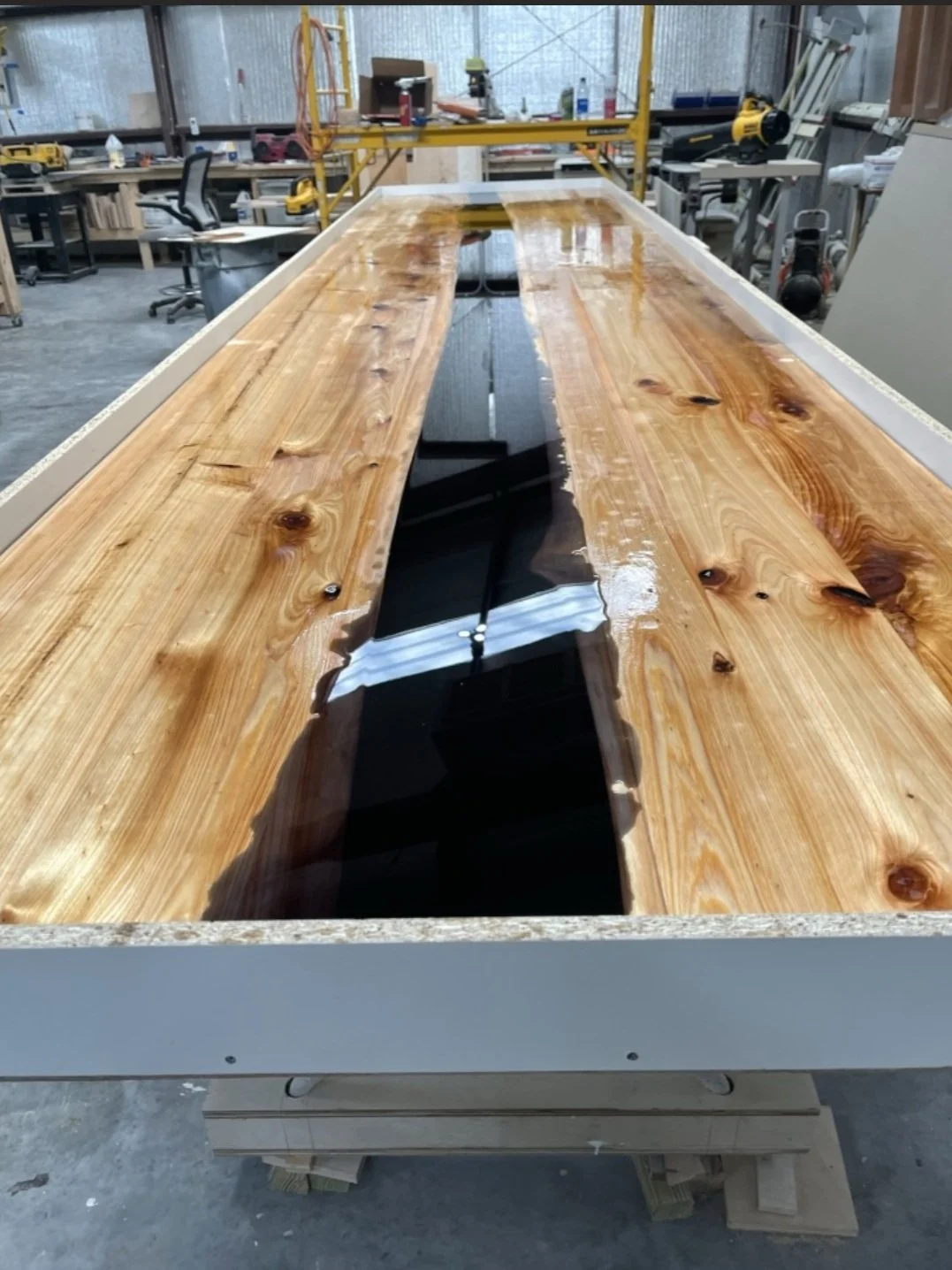 Wooden table with a center strip of black resin in a woodworking workshop.