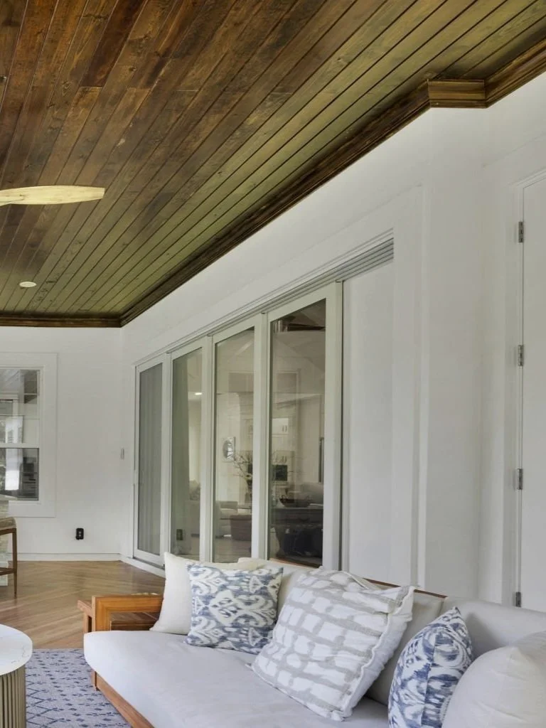 Living room with white sofa, decorative pillows, wooden ceiling, glass sliding doors, and wooden flooring.