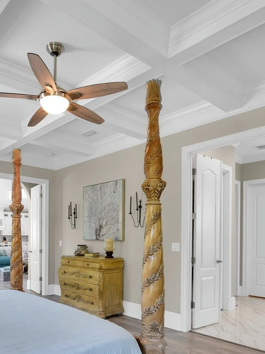 A bedroom with a ceiling fan, a wooden dresser, wall sconces, framed art, and ornate bedposts