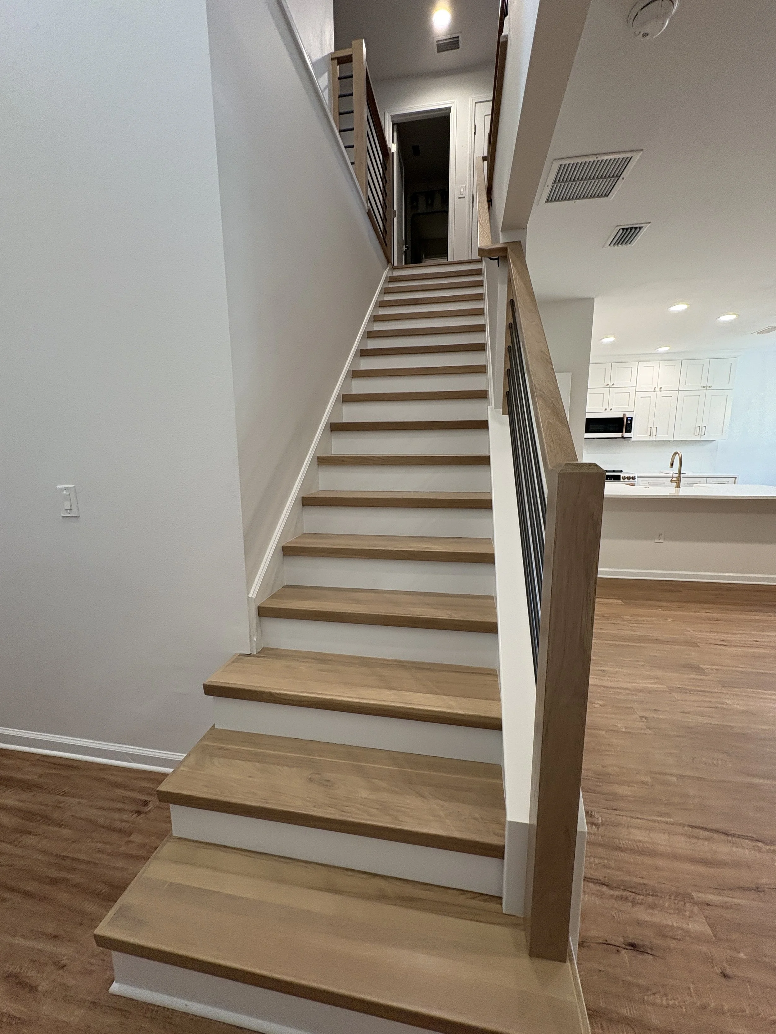 This custom staircase renovation features warm wood treads, crisp white risers, and modern metal railings, creating a striking centerpiece in this high-end Jacksonville condo remodel by Elite Construction of JAX.