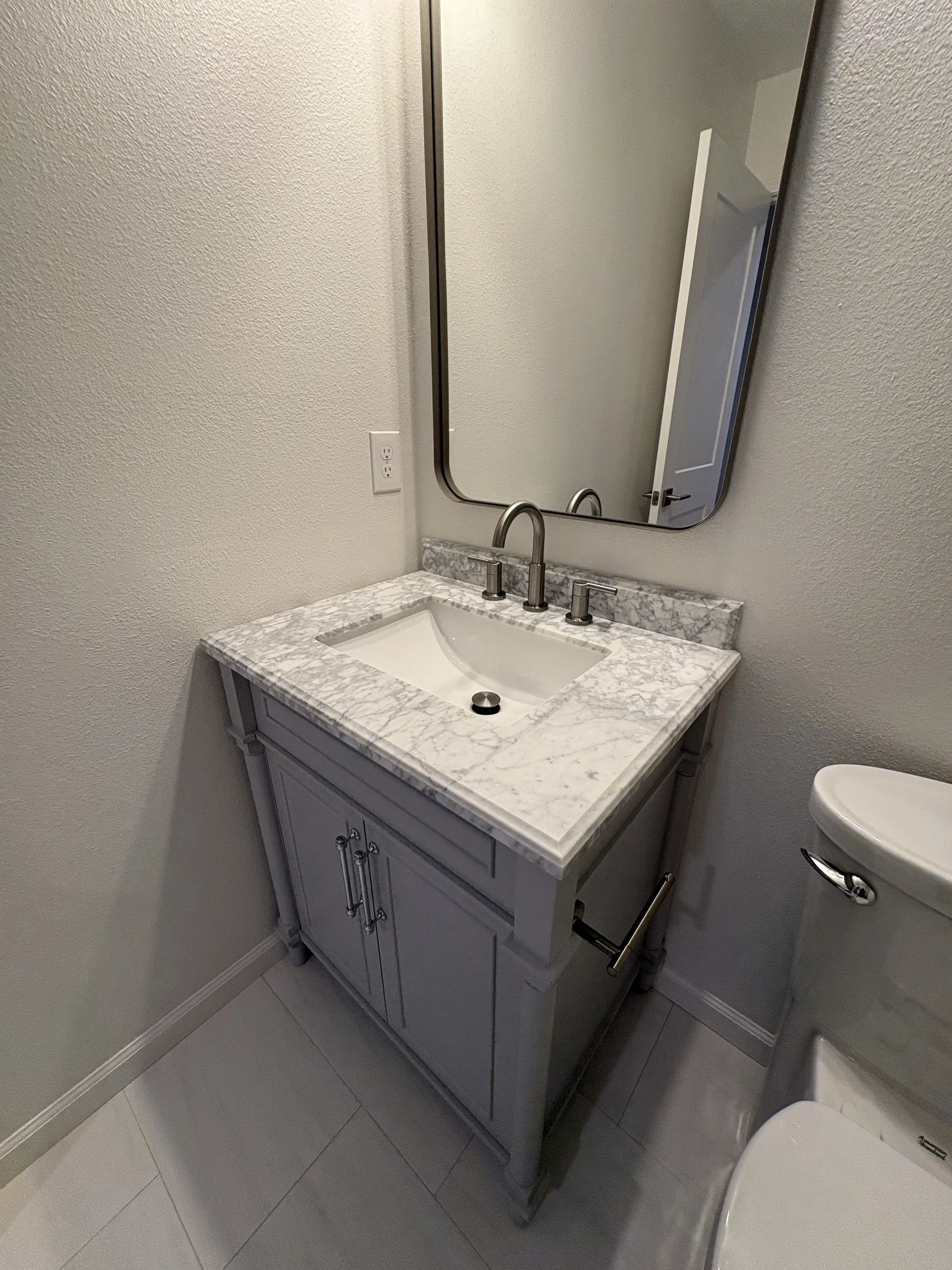 A custom gray vanity with a marble-look countertop and contemporary mirror brings polished style and practical storage to this high-end Jacksonville condo bathroom remodel by Elite Construction of JAX.