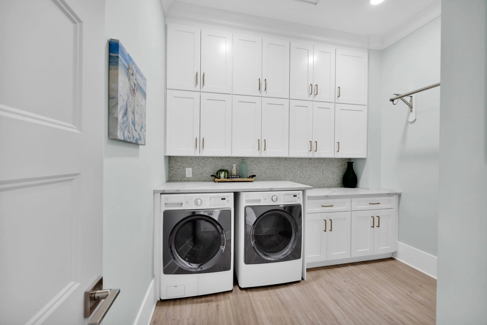 A laundry room with white cabinetry, a countertop, a washer and dryer, a small piece of art on the wall, and decorative items like vases and plants.