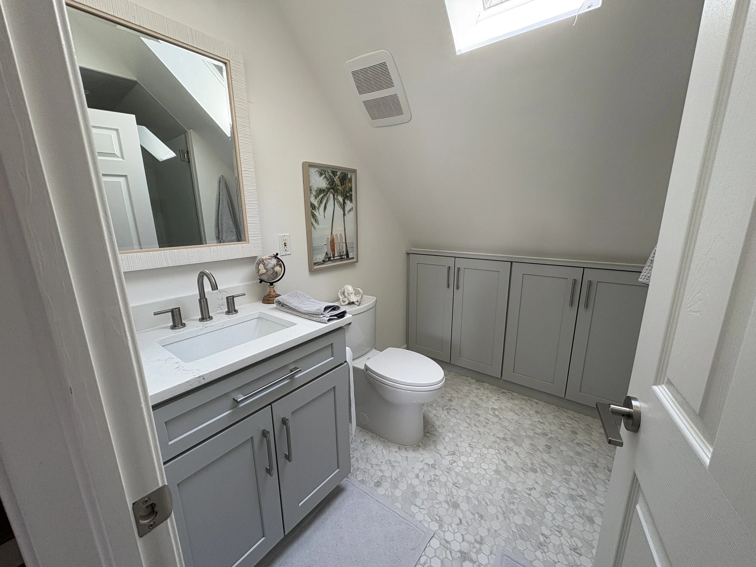 Finished guest bathroom featuring a custom gray shaker vanity with quartz countertops, brushed bronze fixtures, and an oversized framed mirror that enhances the room’s bright, open feel. Additional built-in storage cabinetry maximizes organization an