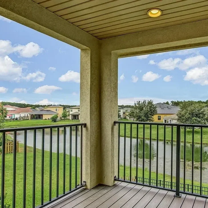 View from a balcony overlooking a pond with green grass and houses in the background, under a partly cloudy sky.