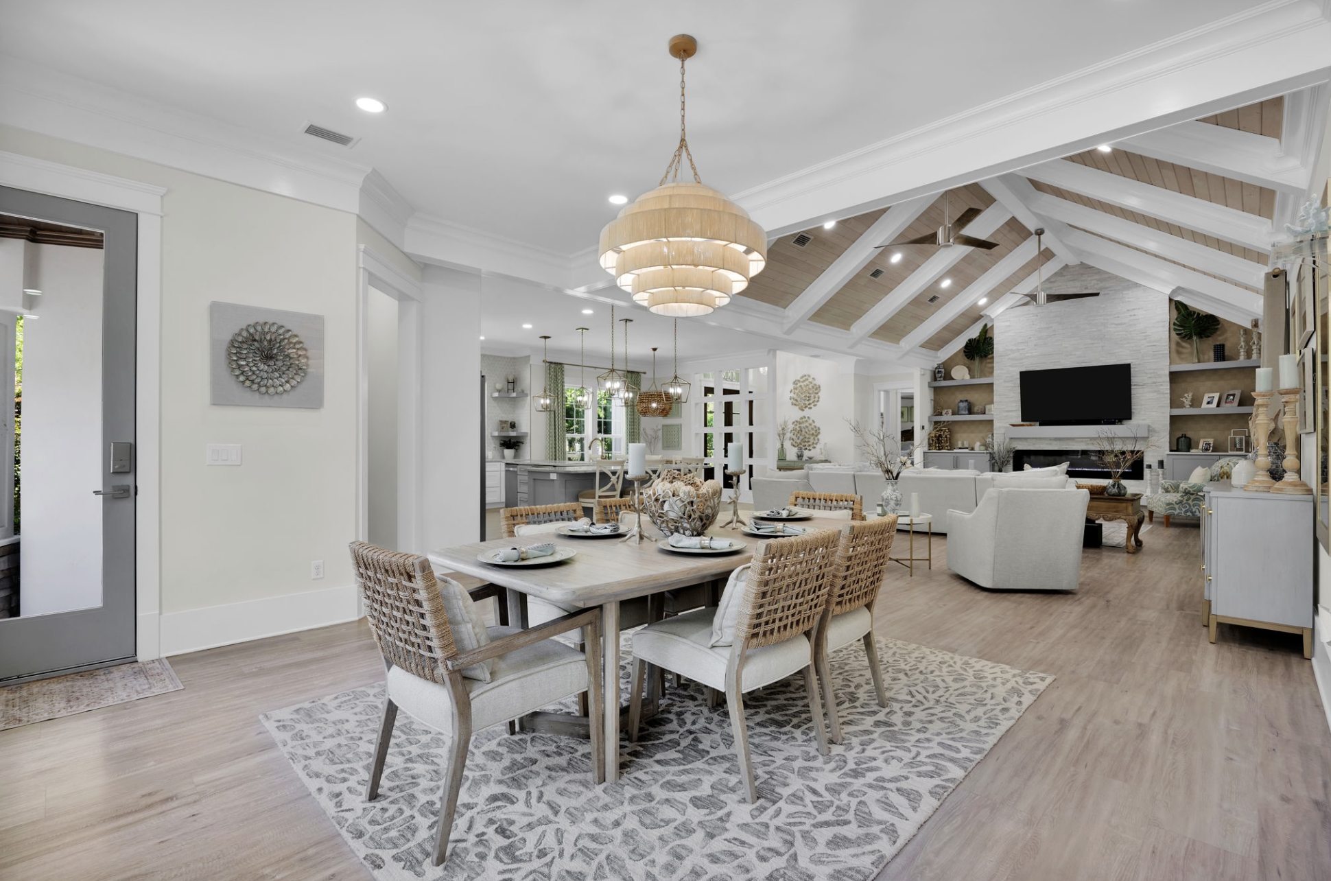 Open concept living and dining area with a wooden dining table set for dinner, a chandelier overhead, and a spacious living room with a flat-screen TV and cream-colored furniture.