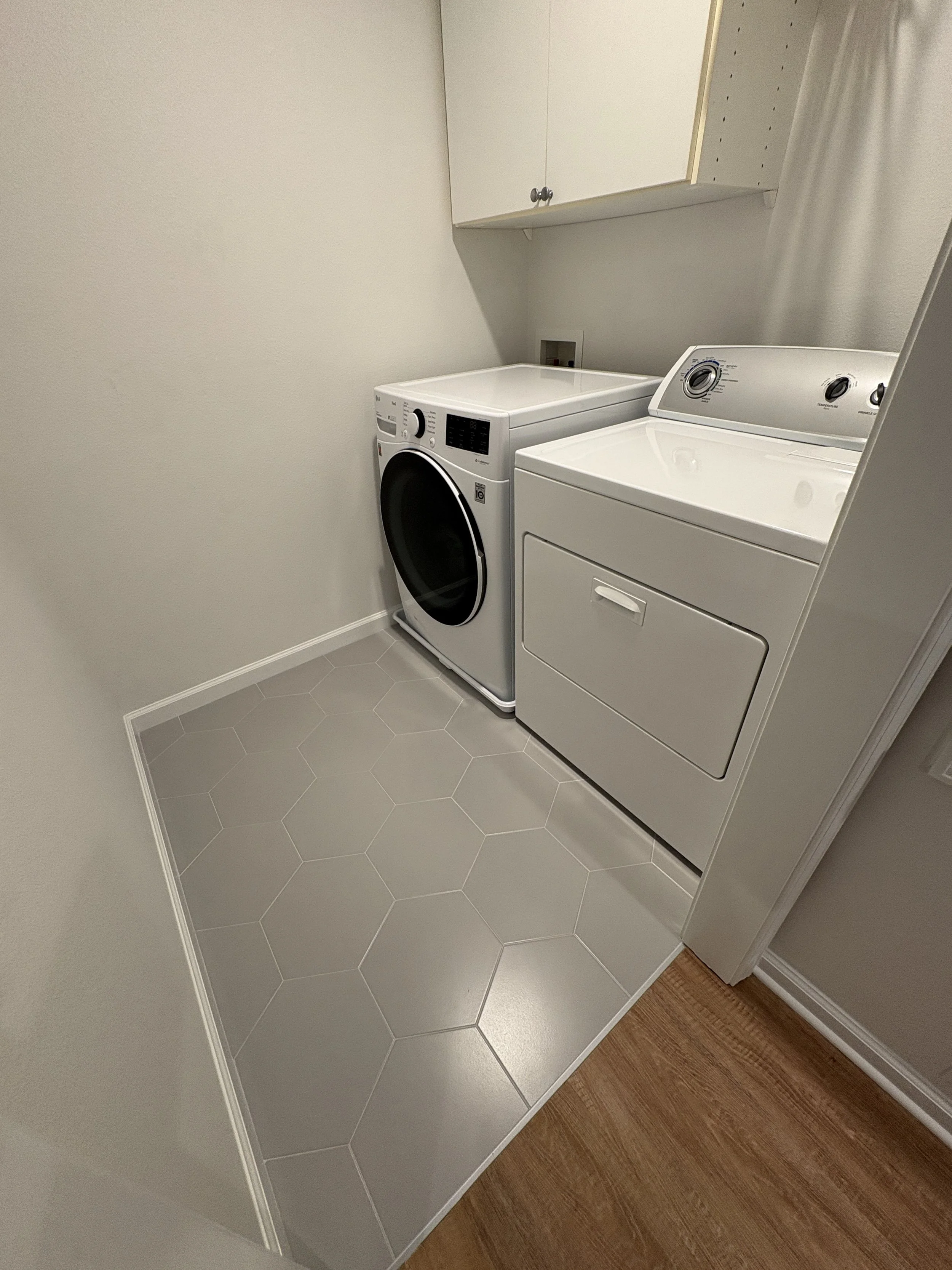 This updated laundry room features modern tile flooring, clean finishes, overhead storage, and a streamlined washer and dryer setup as part of a high-end full-condo remodel in Jacksonville, Florida, by Elite Construction of JAX.