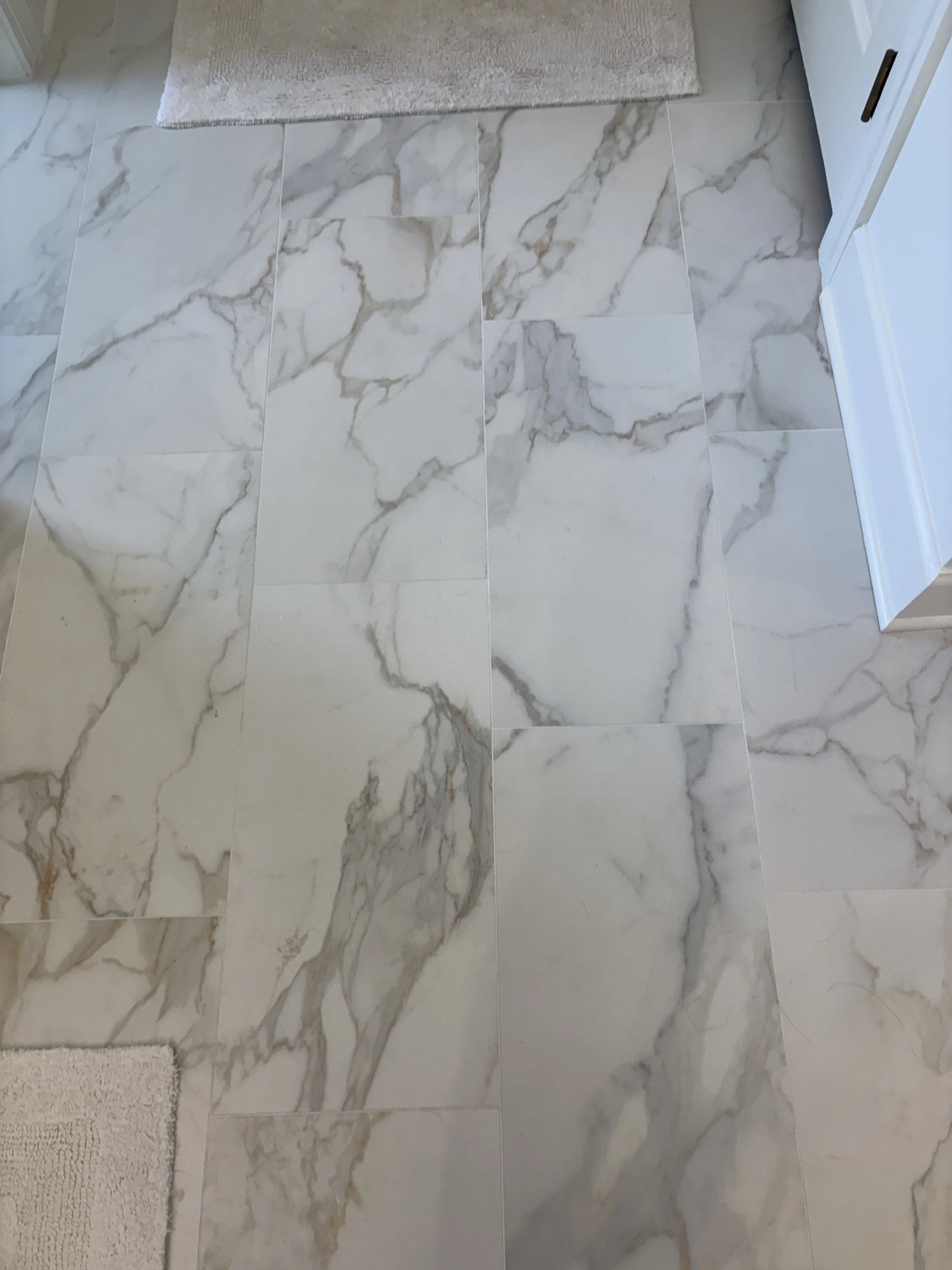 Finished primary bathroom featuring large-format marble-look porcelain tile flooring with dramatic natural veining that adds depth, texture, and timeless elegance to the space. The seamless tile installation enhances the room’s open, luxurious feel w