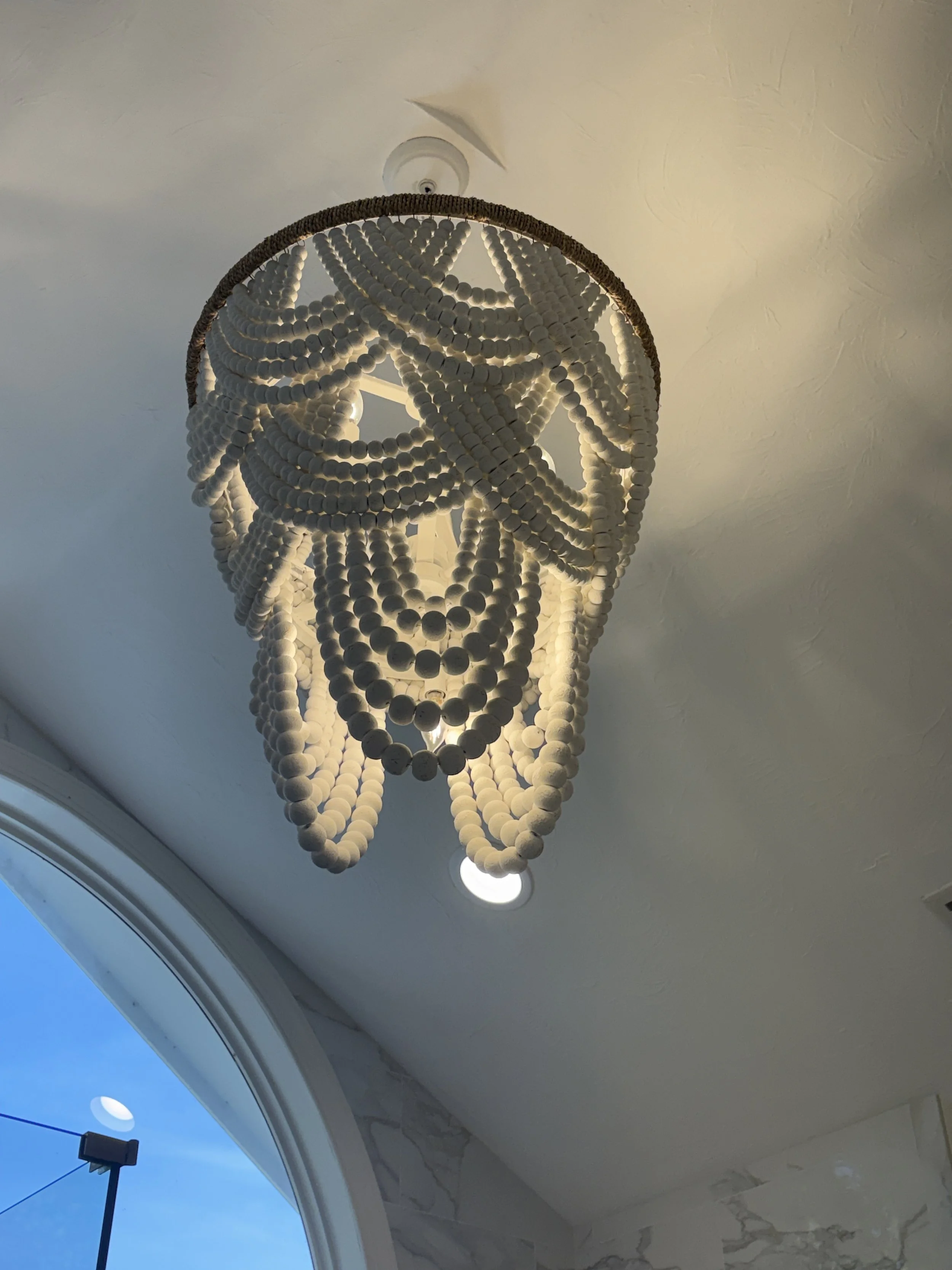 Finished primary bathroom featuring a statement chandelier with cascading bead detailing that serves as a striking focal point within the vaulted ceiling design. Positioned above the luxury bathing area, the decorative lighting enhances the room’s el