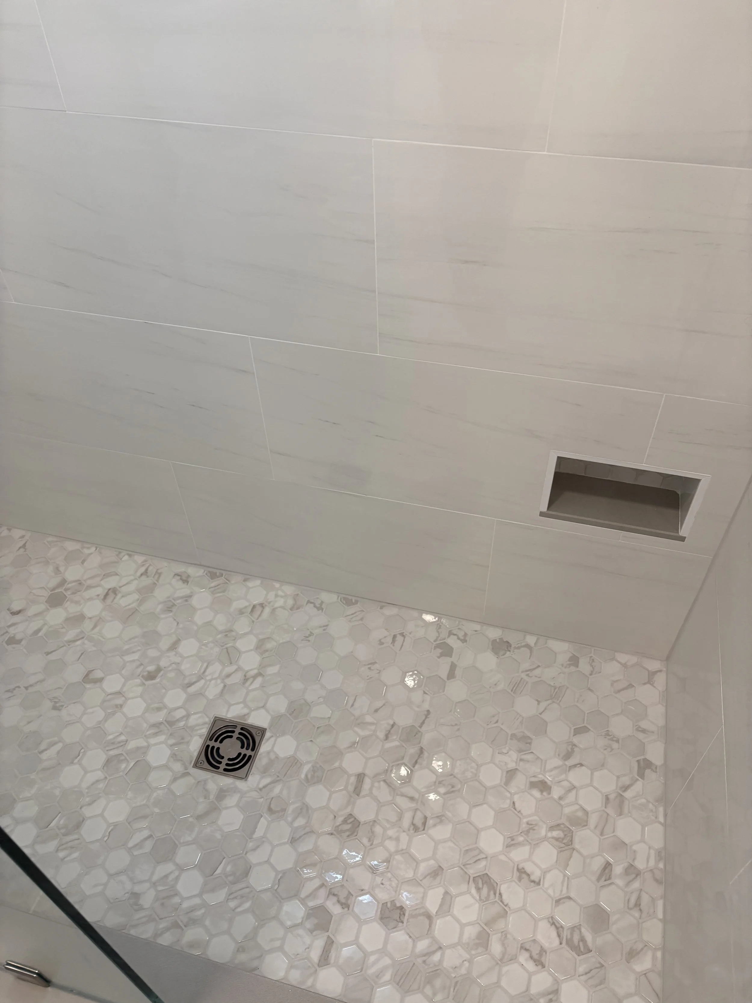 Finished custom walk-in shower featuring a mosaic tile shower floor, large-format wall tile, and a recessed shower niche that combines practical storage with a clean, streamlined appearance. The durable tile selections, precise installation, and neut