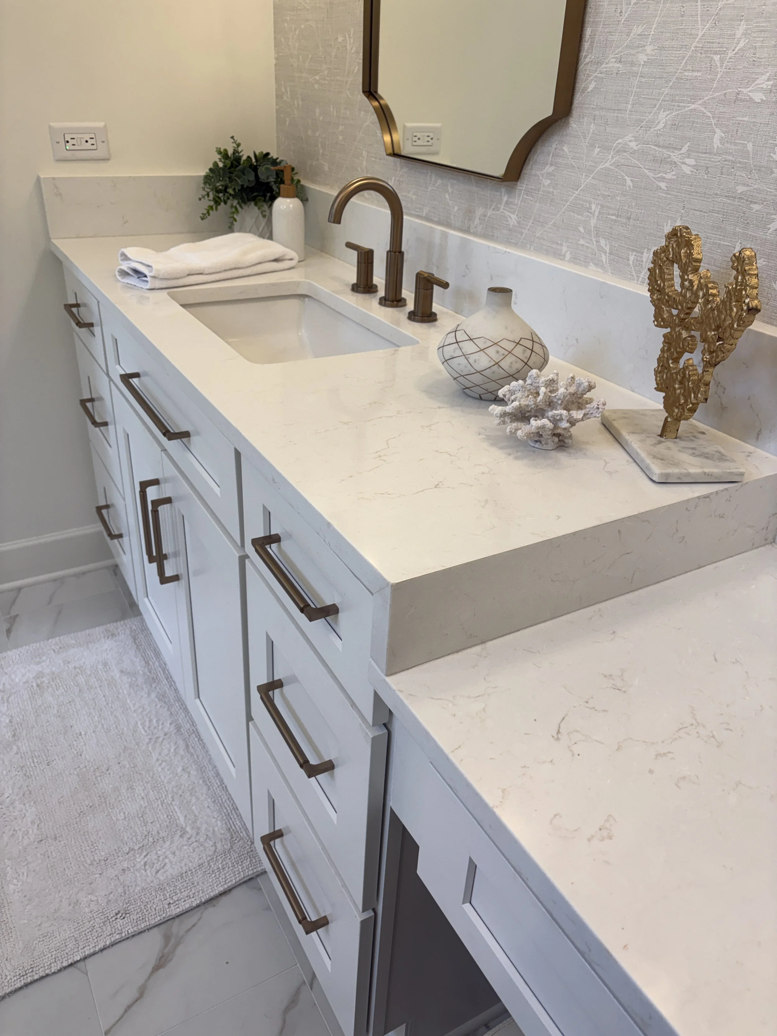 Finished primary bathroom vanity featuring custom white shaker cabinetry, quartz countertops, and an integrated undermount sink designed for lasting beauty and everyday functionality. Premium bronze fixtures, polished hardware, and elegant decorative
