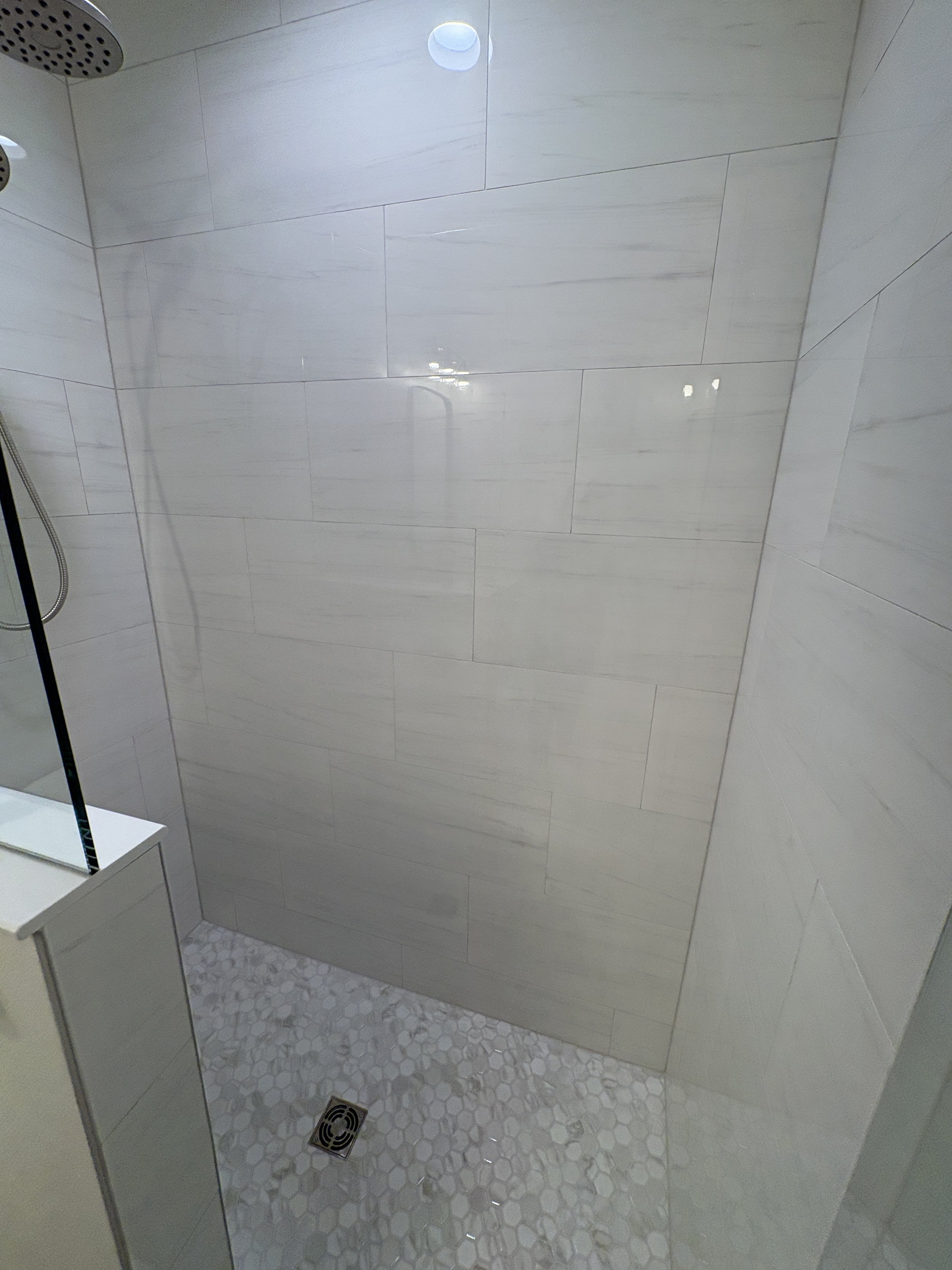 This custom walk-in shower features marble-look wall tile, a coordinating mosaic floor, and a frameless glass enclosure, creating a bright and elegant addition to this high-end Jacksonville condo bathroom remodel by Elite Construction of JAX.