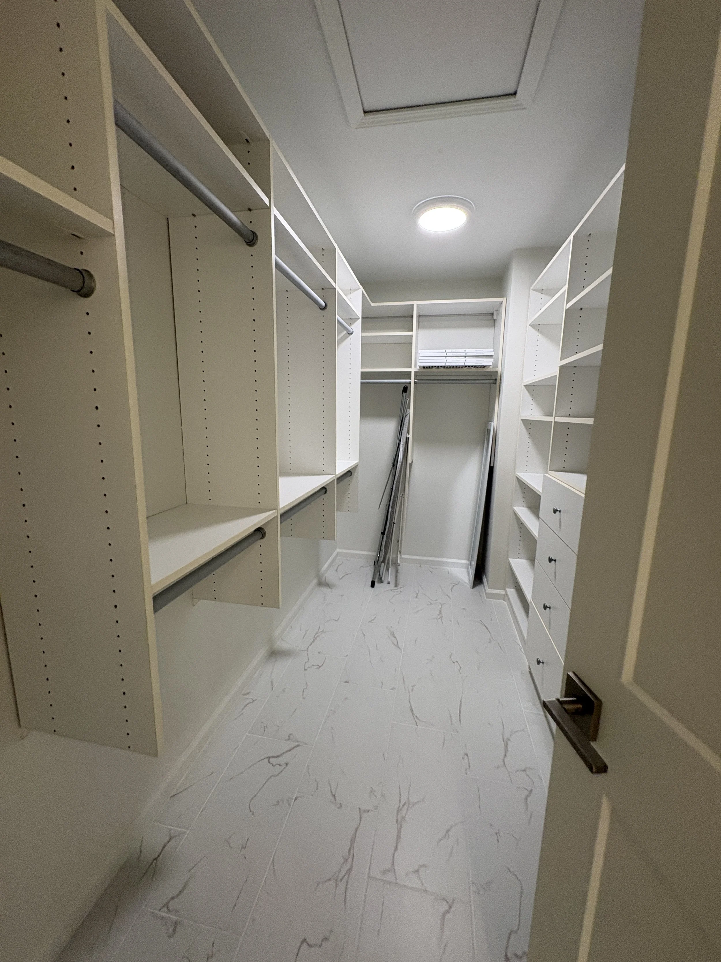 This spacious custom walk-in closet features built-in shelving, hanging storage, and marble-look tile flooring as part of a high-end full-condo remodel in Jacksonville, Florida, by Elite Construction of JAX.