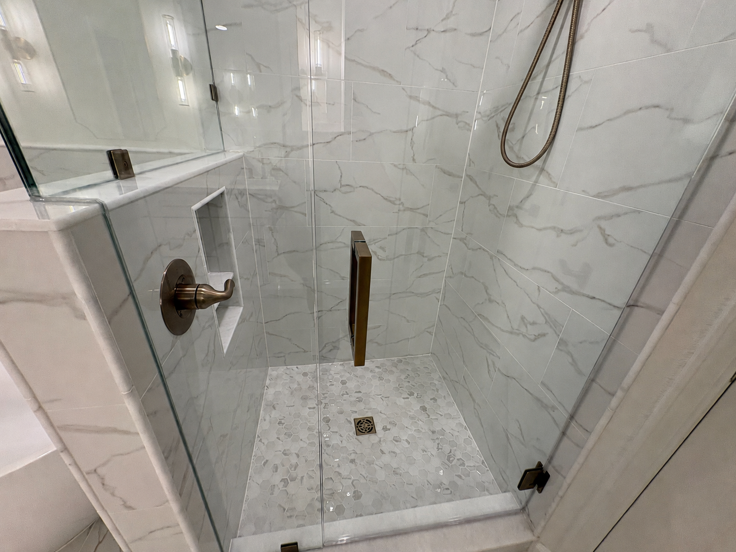 A frameless glass shower with floor-to-ceiling marble-look tile and brushed gold fixtures creates an elegant focal point in this luxury Jacksonville condo bathroom remodel by Elite Construction of JAX.
