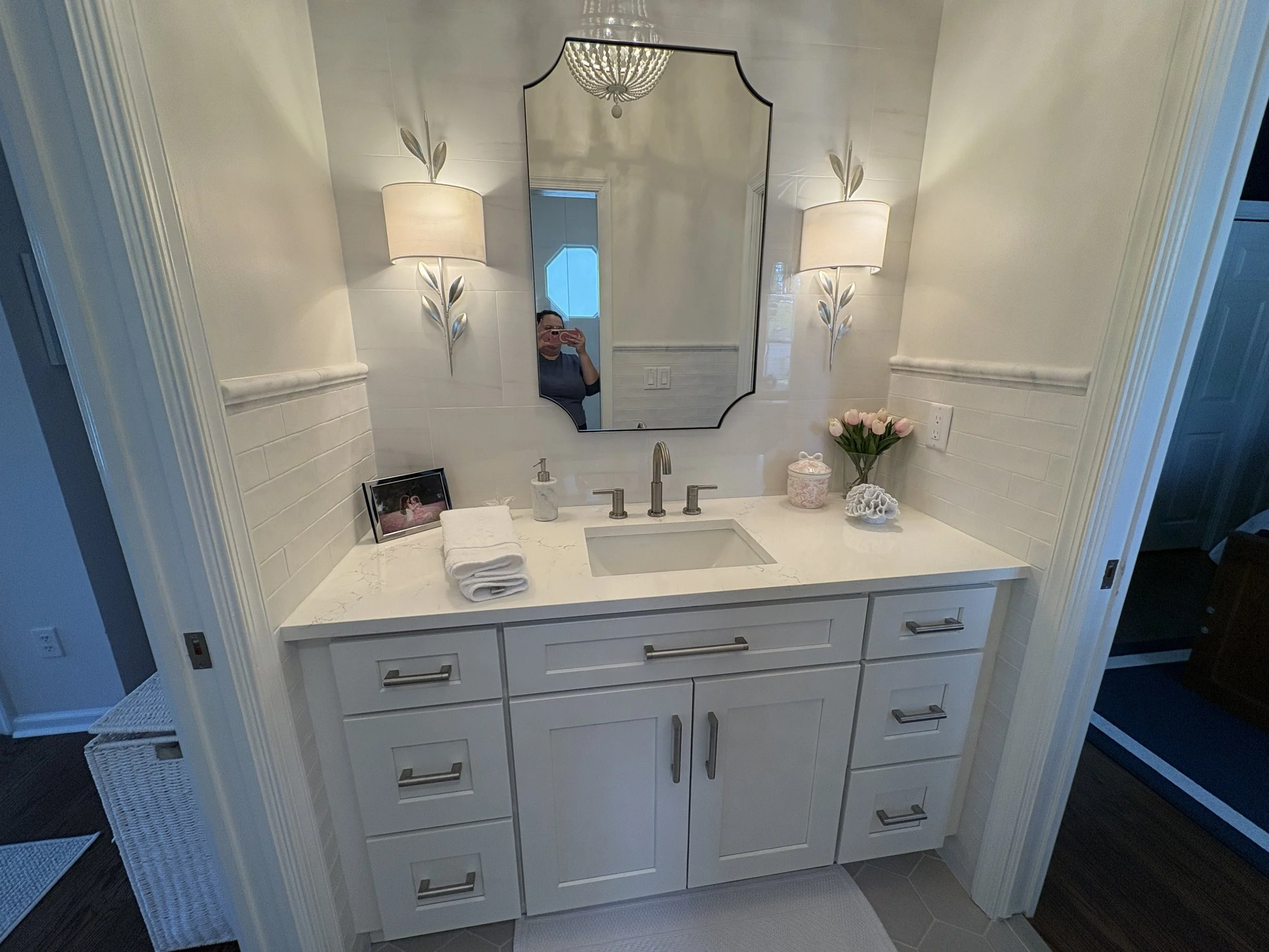 Finished bathroom vanity featuring custom light-gray shaker cabinetry, quartz countertops, and an undermount sink paired with brushed nickel fixtures for a clean, timeless appearance. Decorative wall sconces, a framed mirror, and detailed trim work e