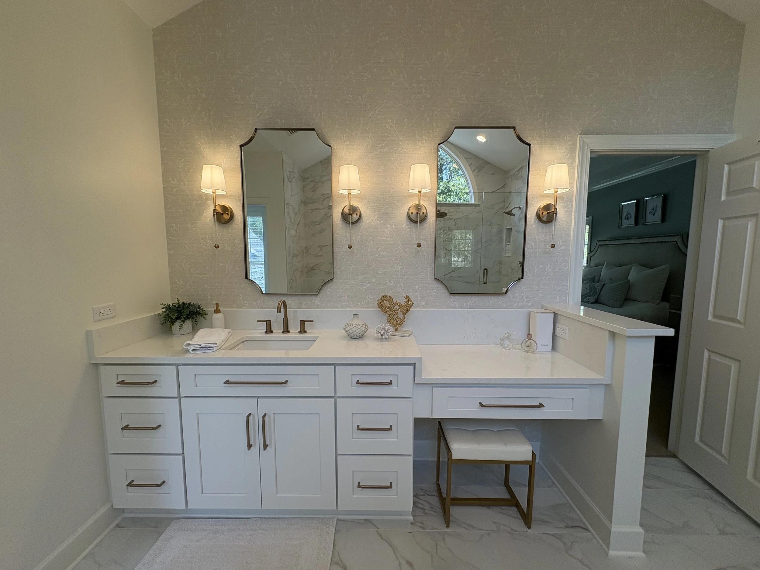 Finished primary bathroom featuring a custom double vanity with white shaker cabinetry, quartz countertops, and integrated storage designed for both beauty and functionality. Elegant wall sconces, decorative mirrors, and a dedicated makeup station cr