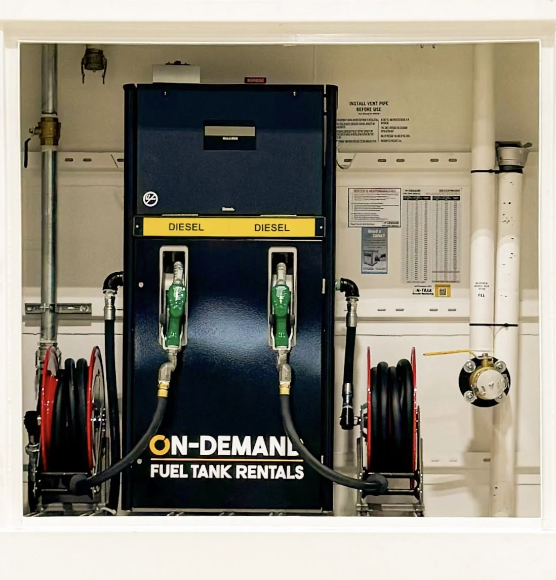 Diesel fuel dispenser with two pumps, green nozzles, and hoses labeled 'On-Demand Fuel Tank Rentals' inside a facility with pipes and equipment.