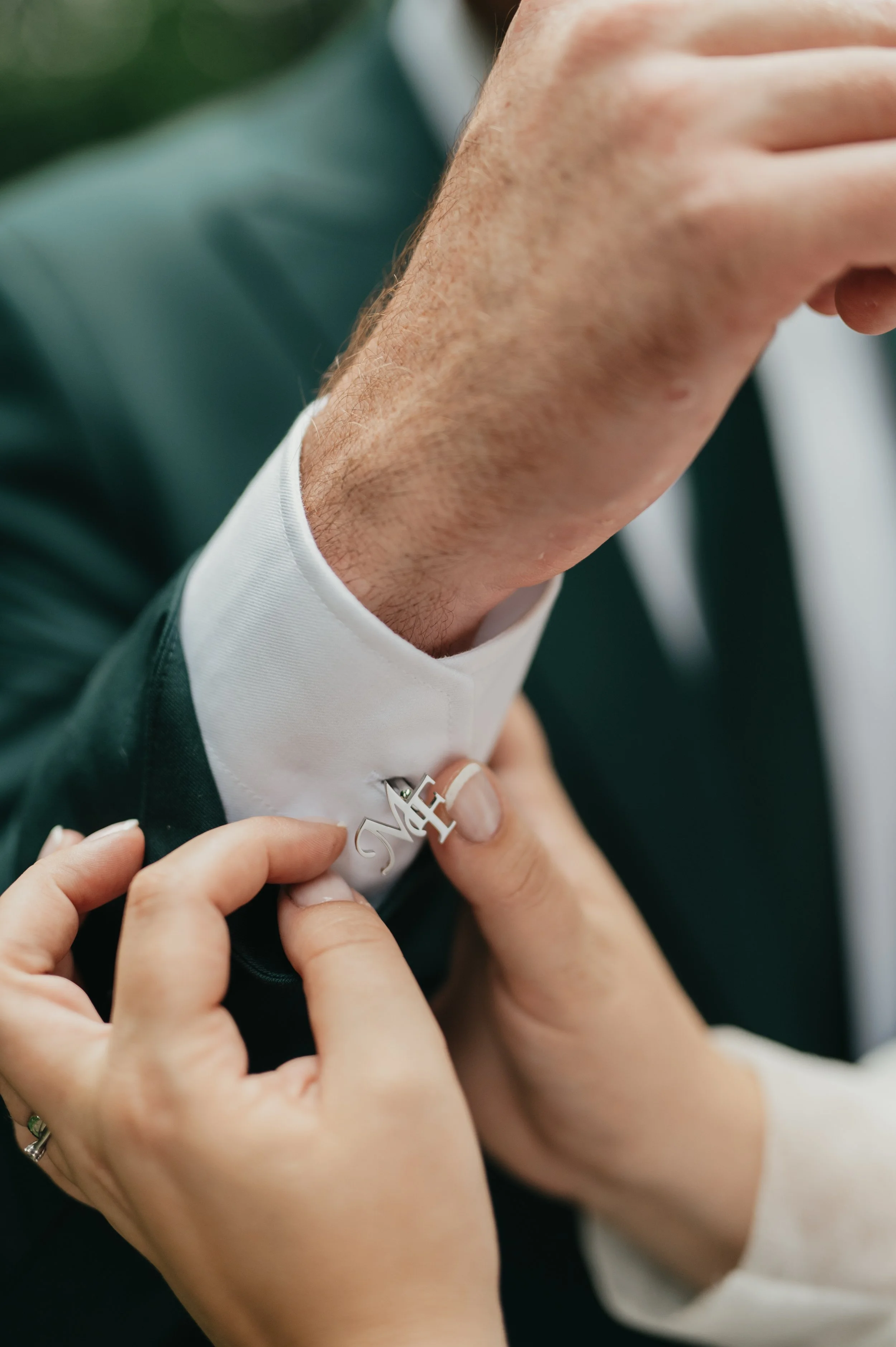 Person adjusting a tie with a letter pin on the collar of a dark suit.