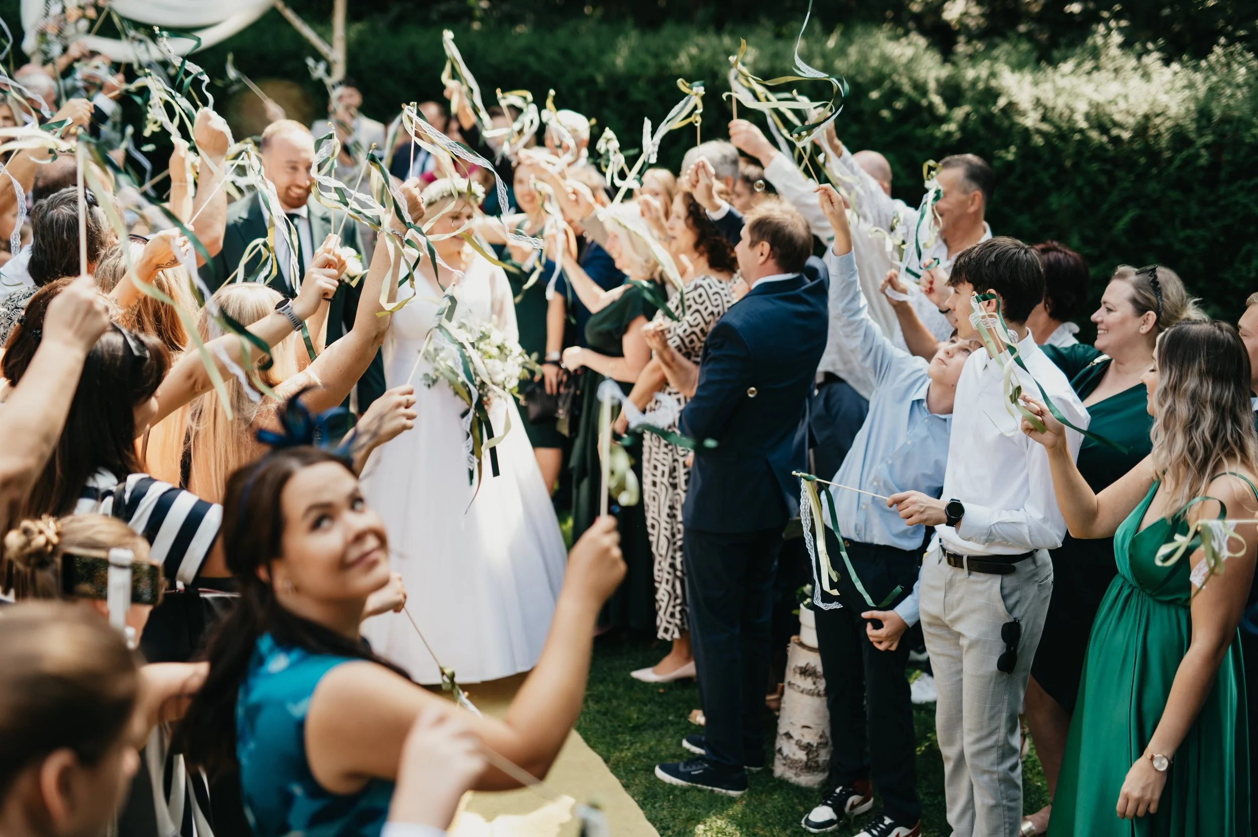 Guests celebrating at a wedding, holding ribbons and cheering outdoors.