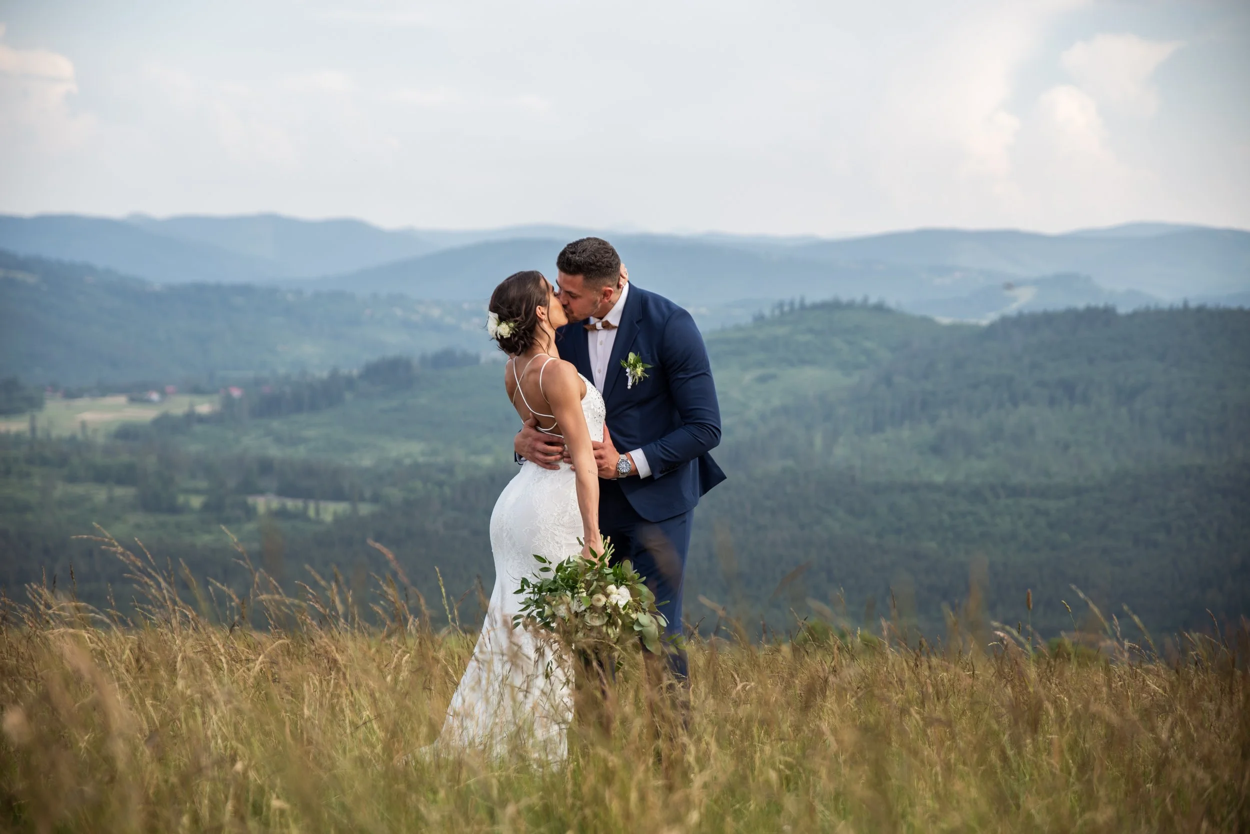 Bride and groom kissing in a field with mountains in the background.