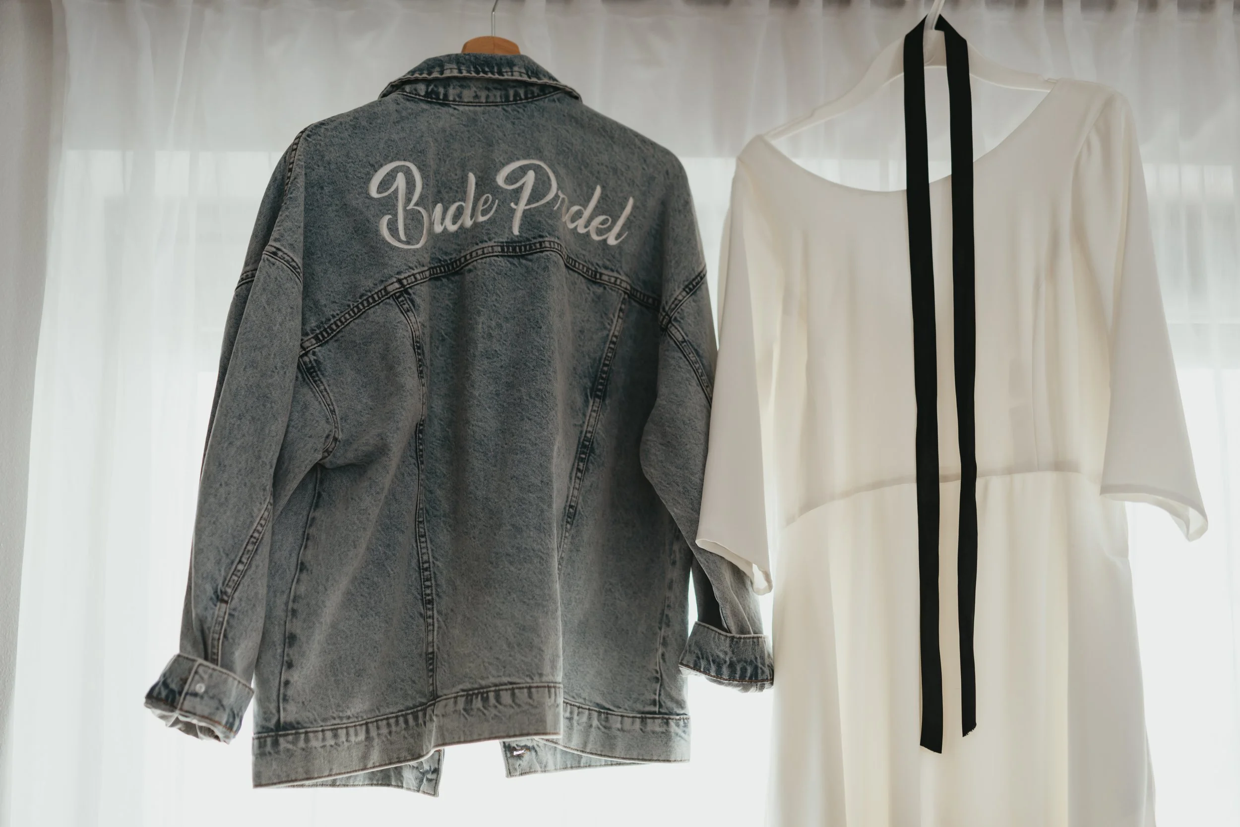 Denim jacket with 'Bride' text and white dress hanging on hangers