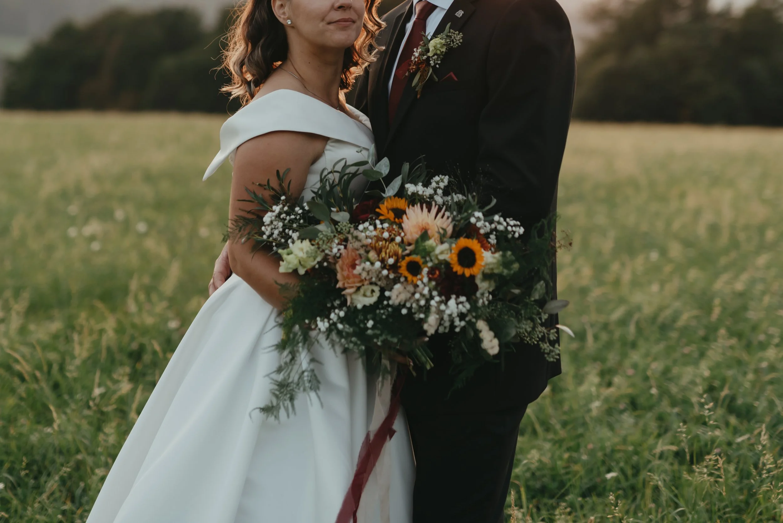 Bride and groom standing in a field, holding a large bouquet of flowers.