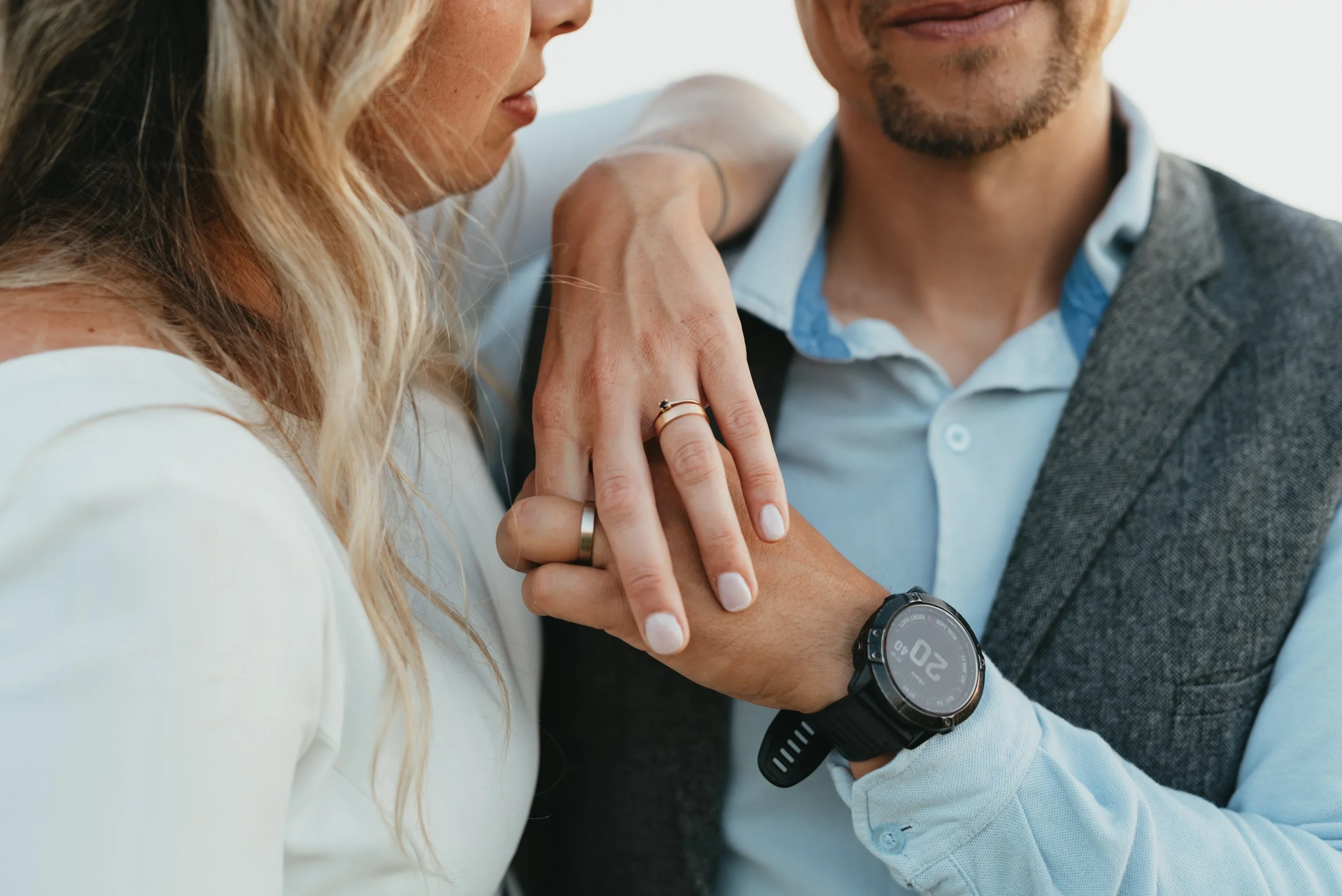 Close-up of a couple holding hands, showing wedding bands and an outdoor watch.