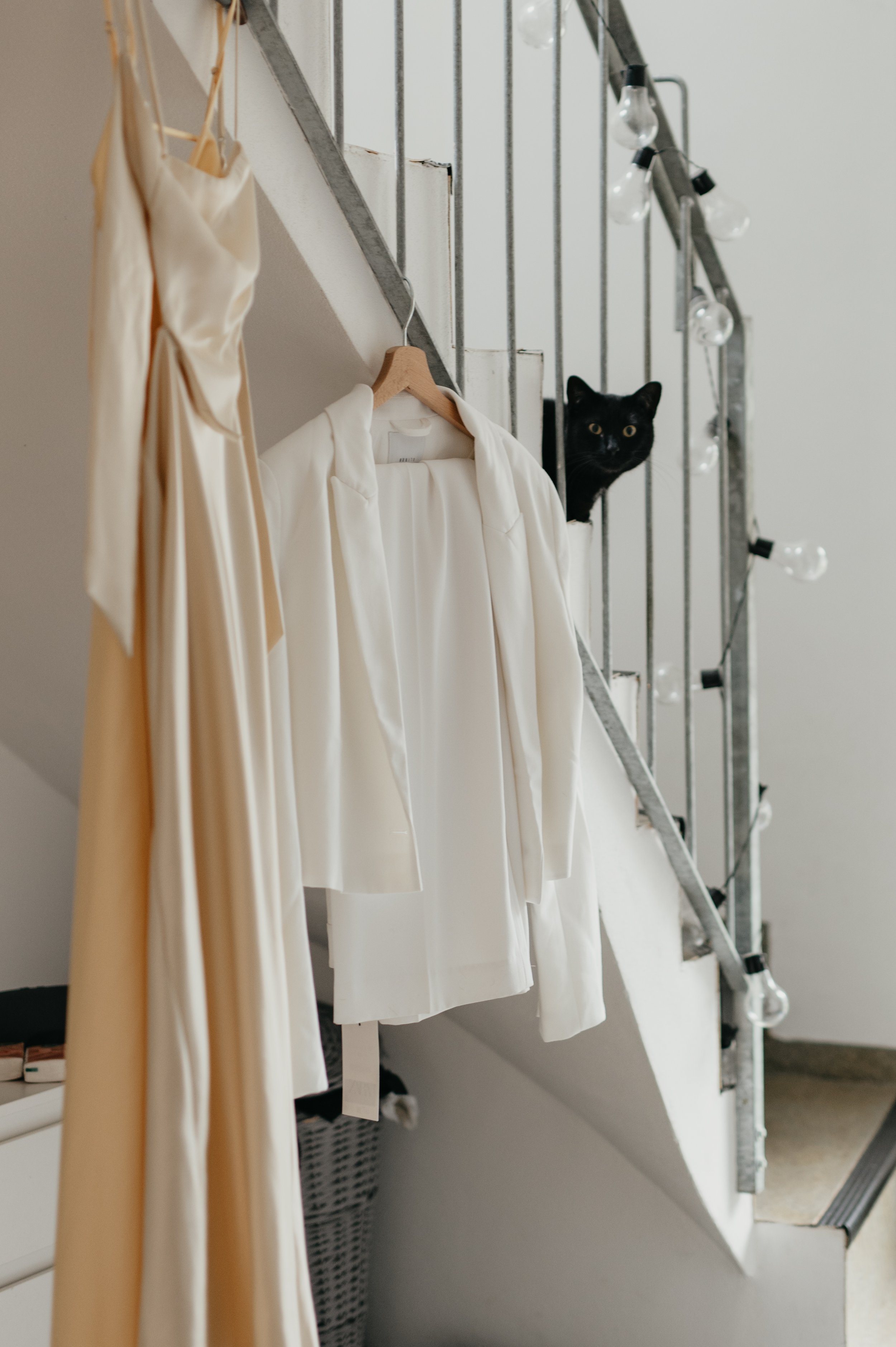 White clothing hanging on a hook under a staircase with a black cat peeking out.