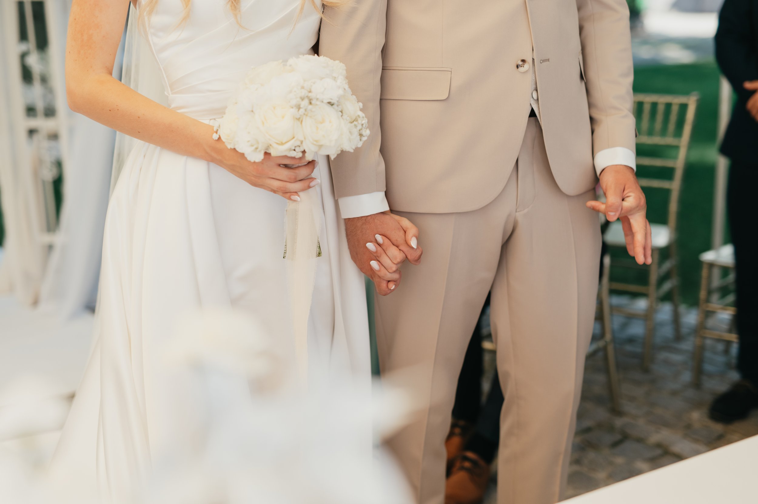 	
Nevěsta a ženich se drží za ruce během svatebního obřadu, nevěsta drží kytici bílých květin.