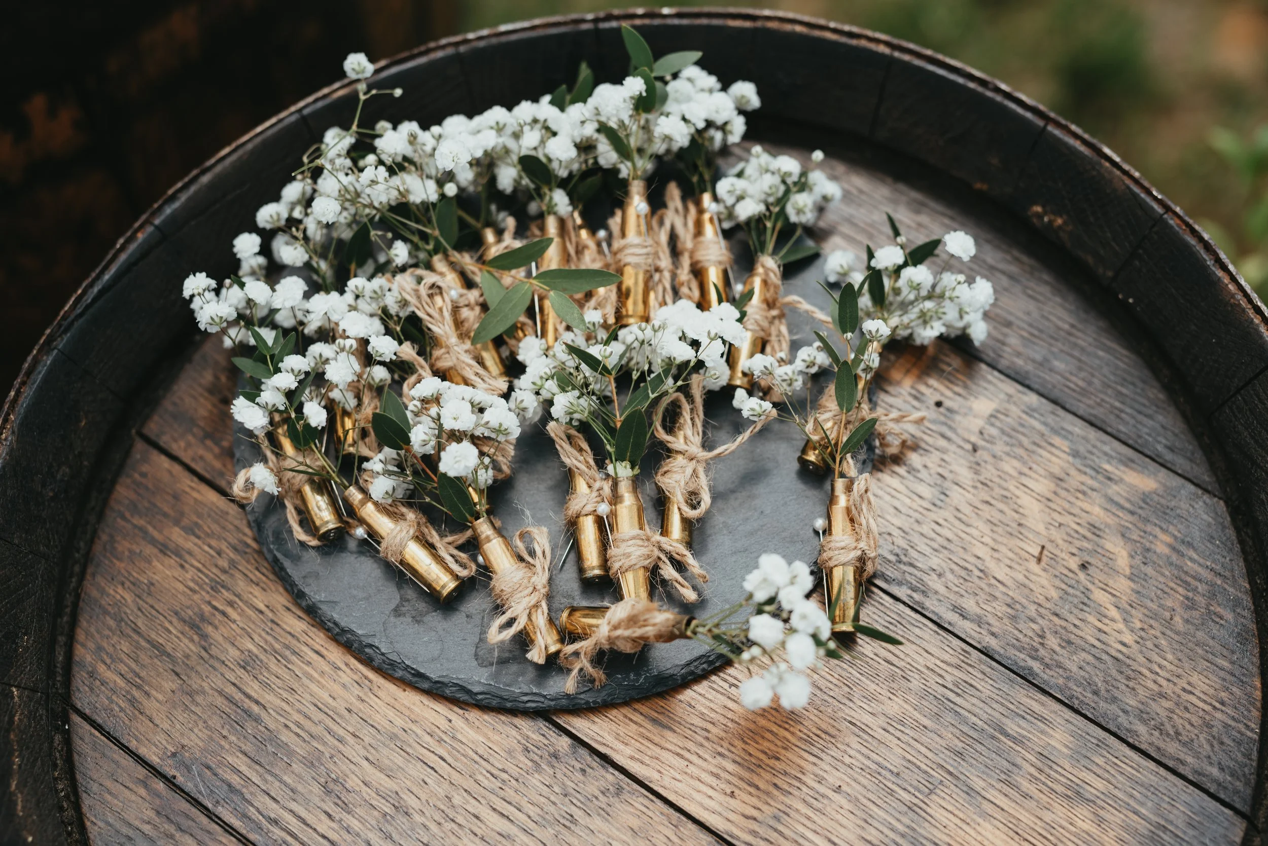 Small arrangements of baby's breath flowers tied with twine to empty bullet casings, displayed on a wooden surface.