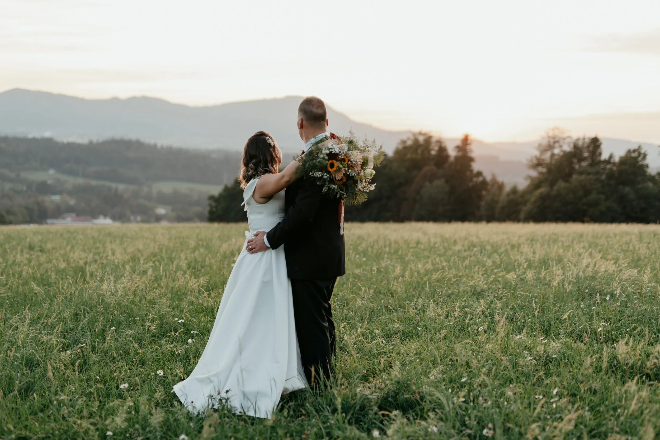 Bride and groom embracing in a field at sunset.