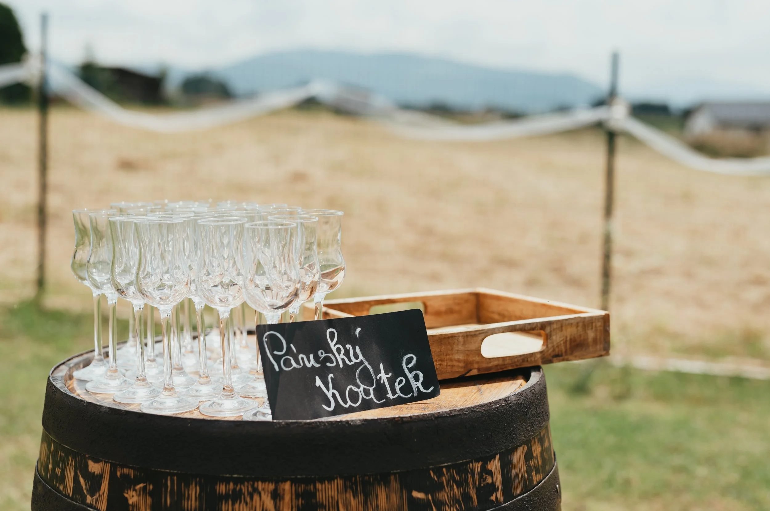 Wine glasses arranged on a barrel with a chalkboard sign outdoors.