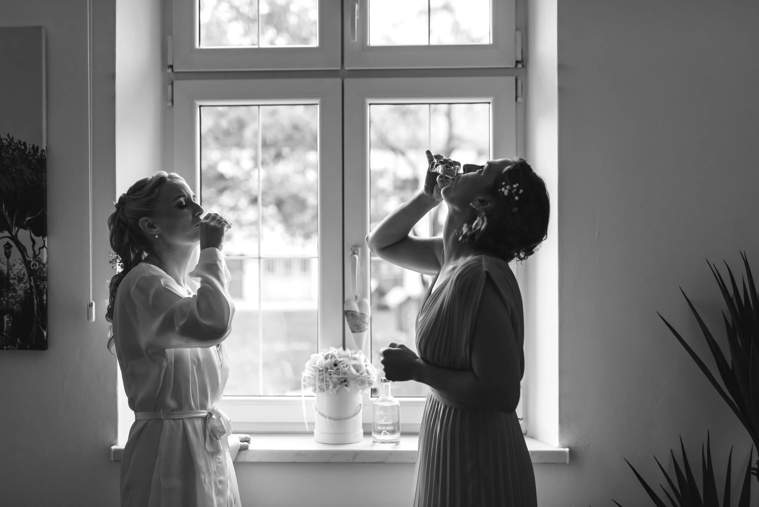 Two women drinking shots in front of a window, black and white photo