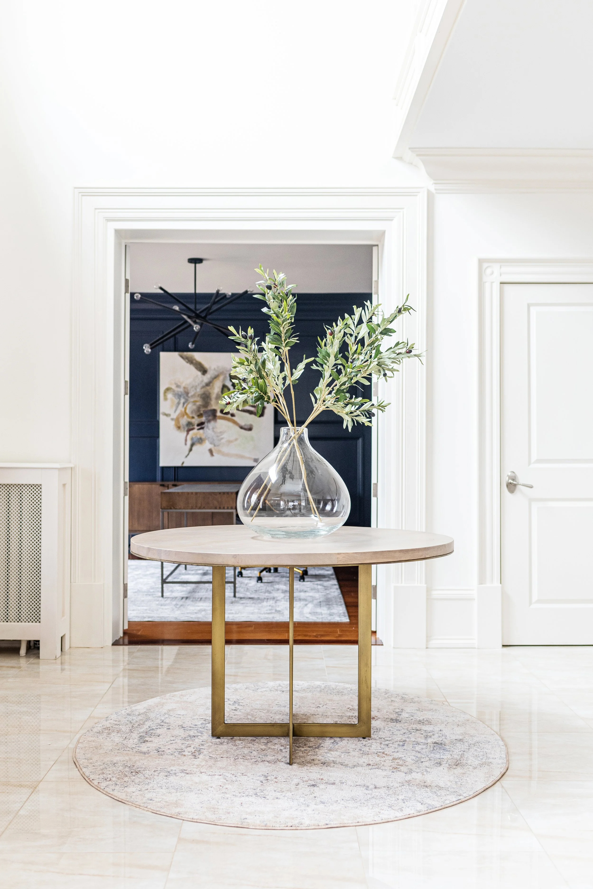 Bright entryway staged with a round table and glass vase of greenery, featuring neutral tones and modern architectural details.
