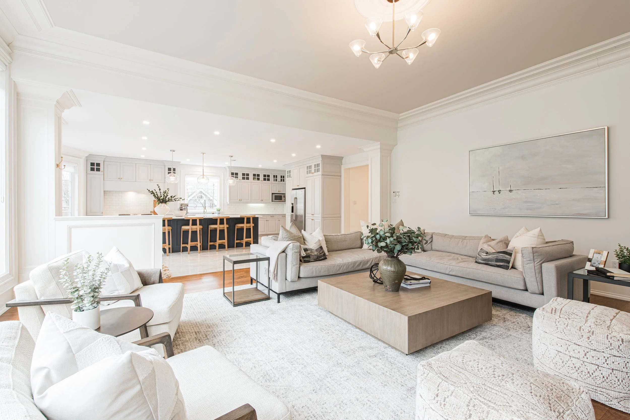 Open-concept living room and kitchen staged in neutral tones with modern furniture, soft textures, and natural greenery — creating a bright and inviting atmosphere.