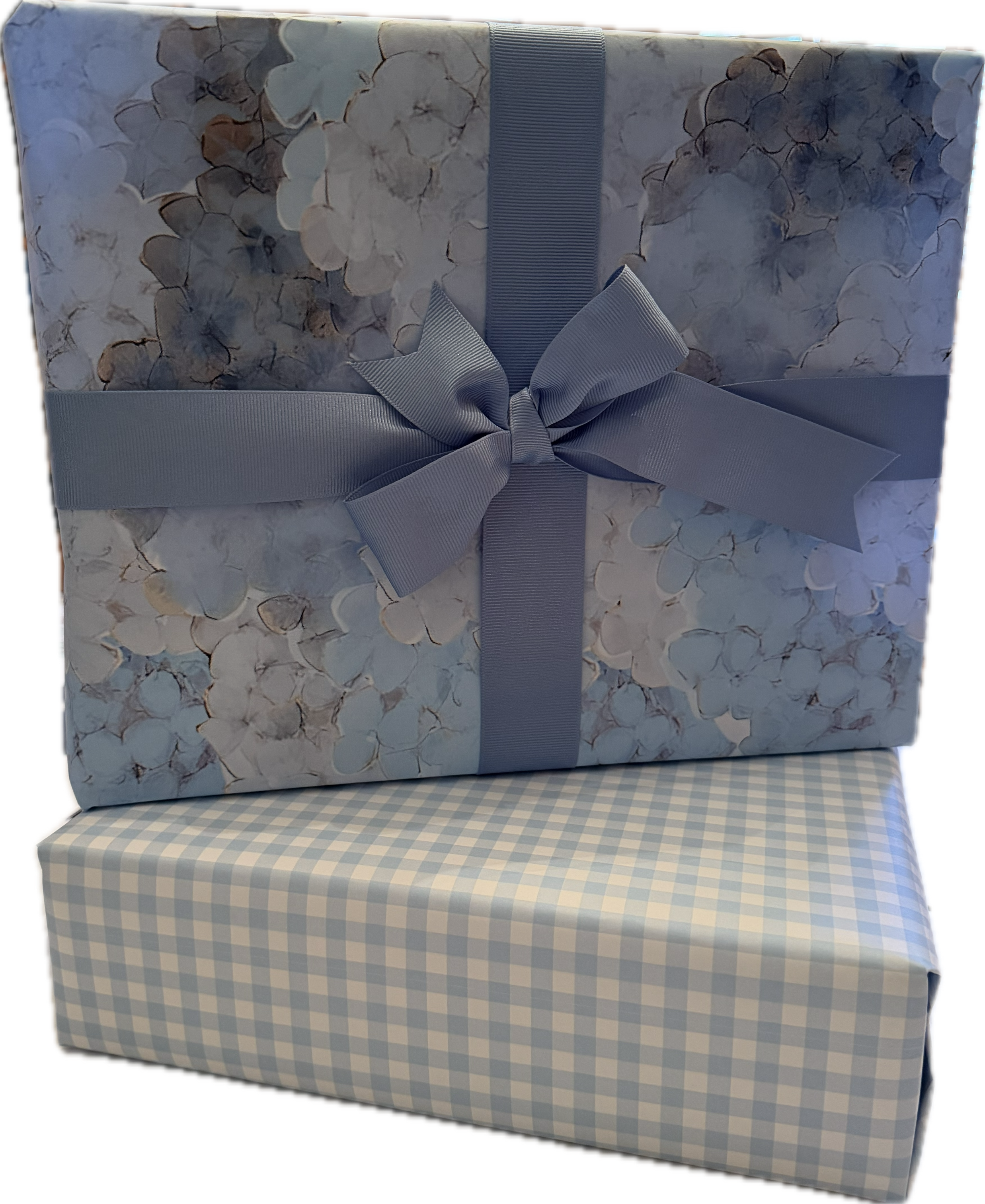 A large gift box wrapped in hydrangea floral paper with different shades of blue, tied with a French Blue ribbon sold 
separately. The smaller box underneath is wrapped in blue and white gingham paper. Luxury wrapping paper sold by Mary Draper Design