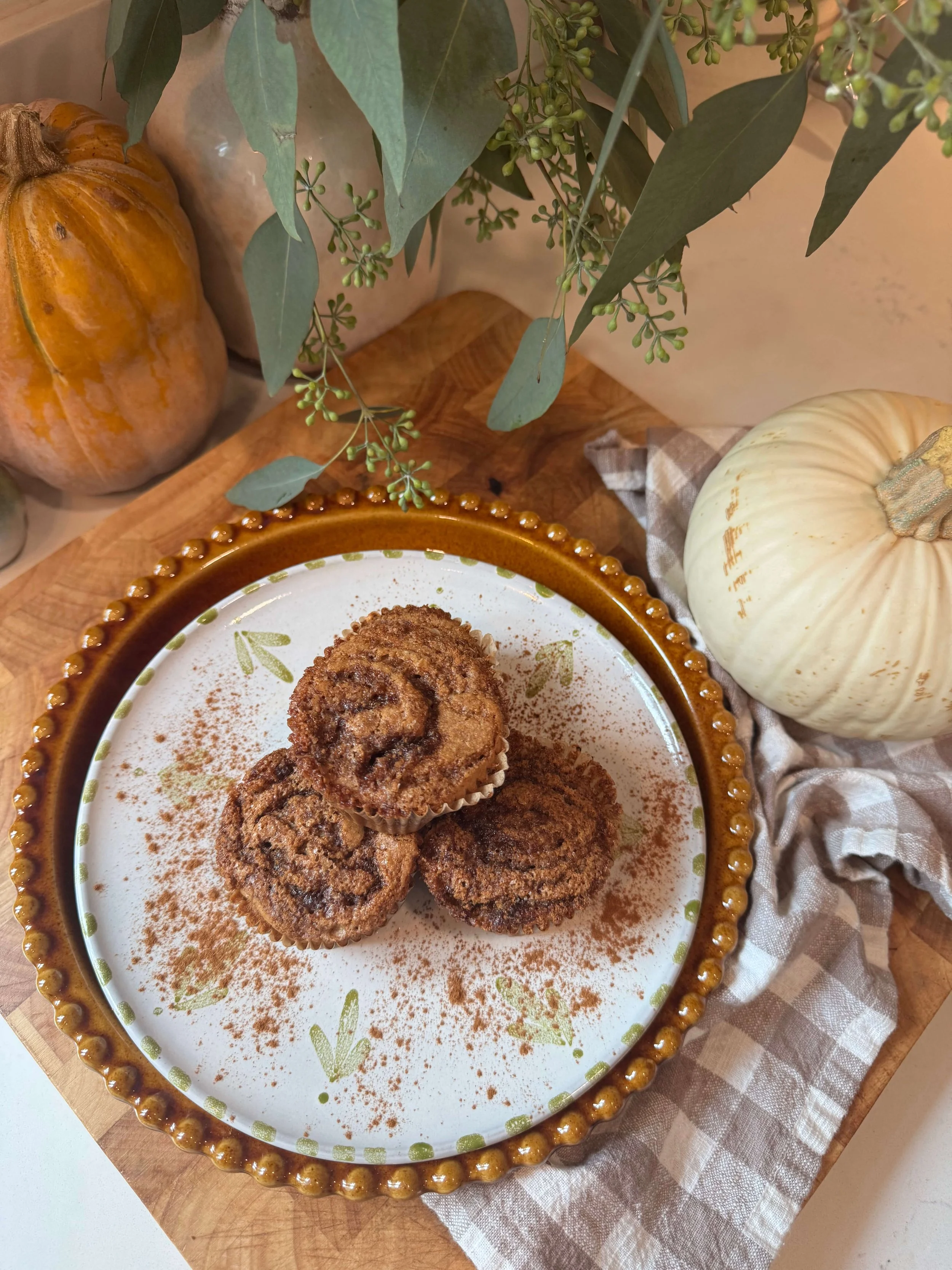 postpartum cinnamon swirl muffins on plate in kitchen with pumpkin