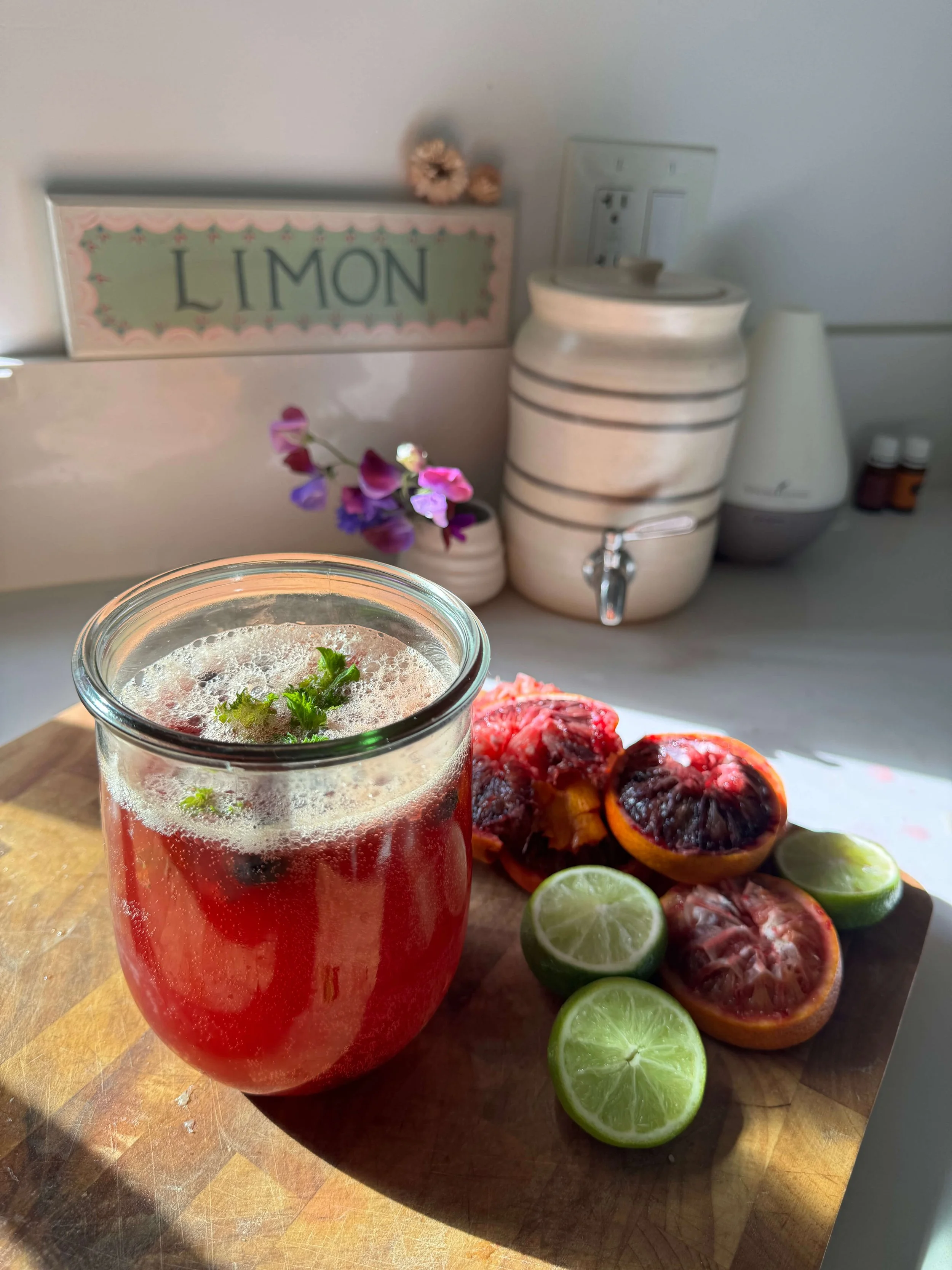 salty lime berry drink in glass with lime and lemon blood orange peeled on kitchen cutting board
